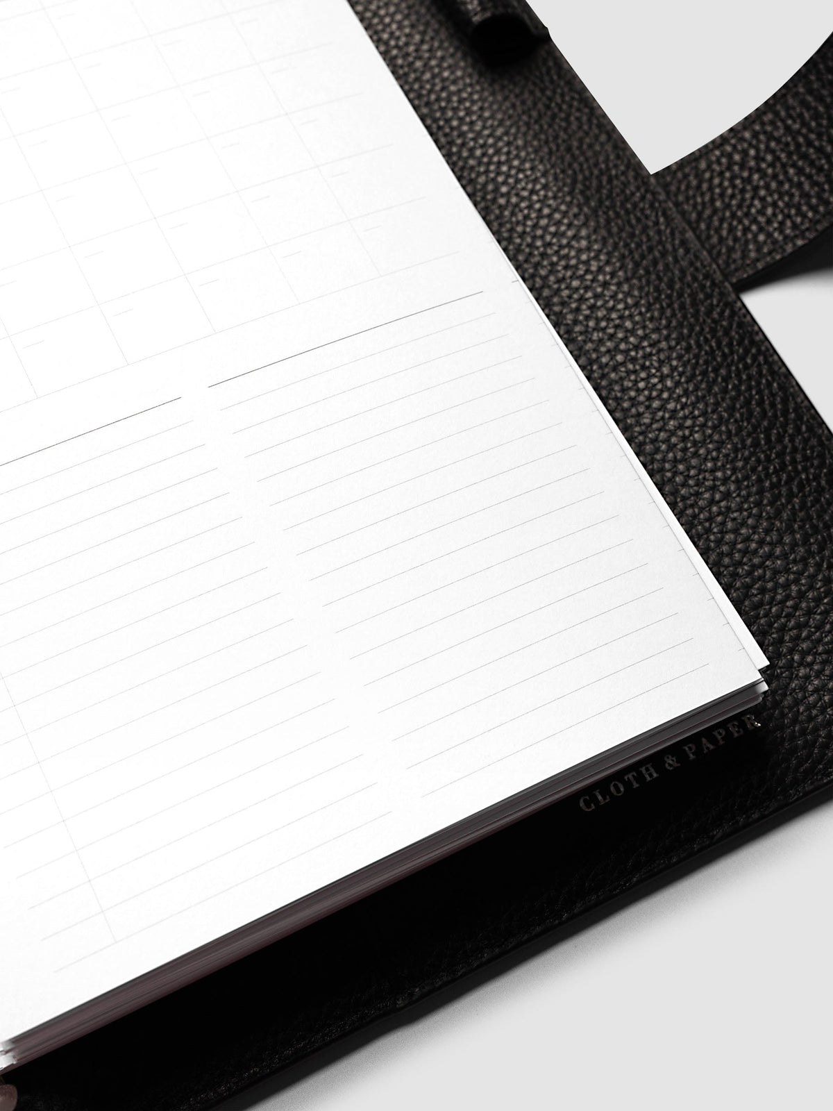 Monthly Fold Out Planner Insert Set of 2, A5 6-Ring Punch, close-up of the lined note columns on the lower half of the page, with the black leather cover and its foil brand mark behind