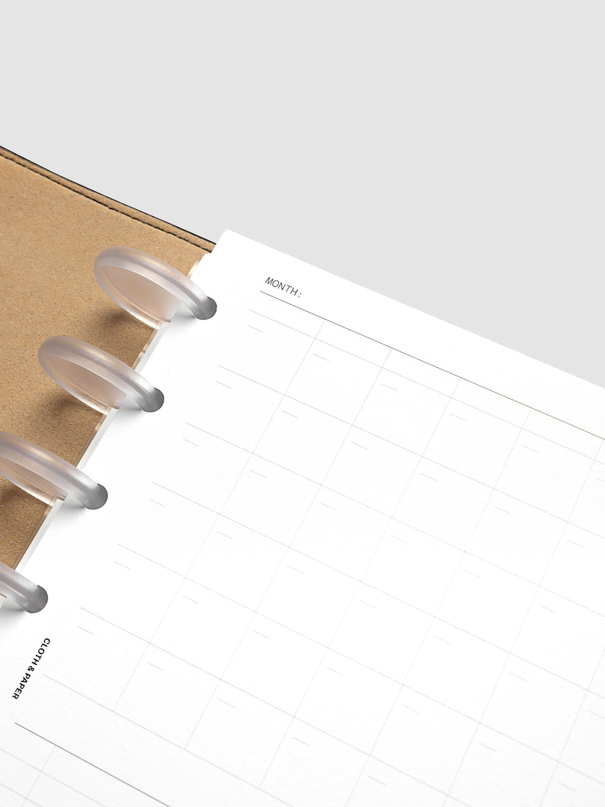 Monthly Fold Out Planner Insert Set of 2, Half Letter 8-Disc Punch, angled close-up of the top left corner, frosted clear discs against the kraft brown cover with the month line and grid beside them