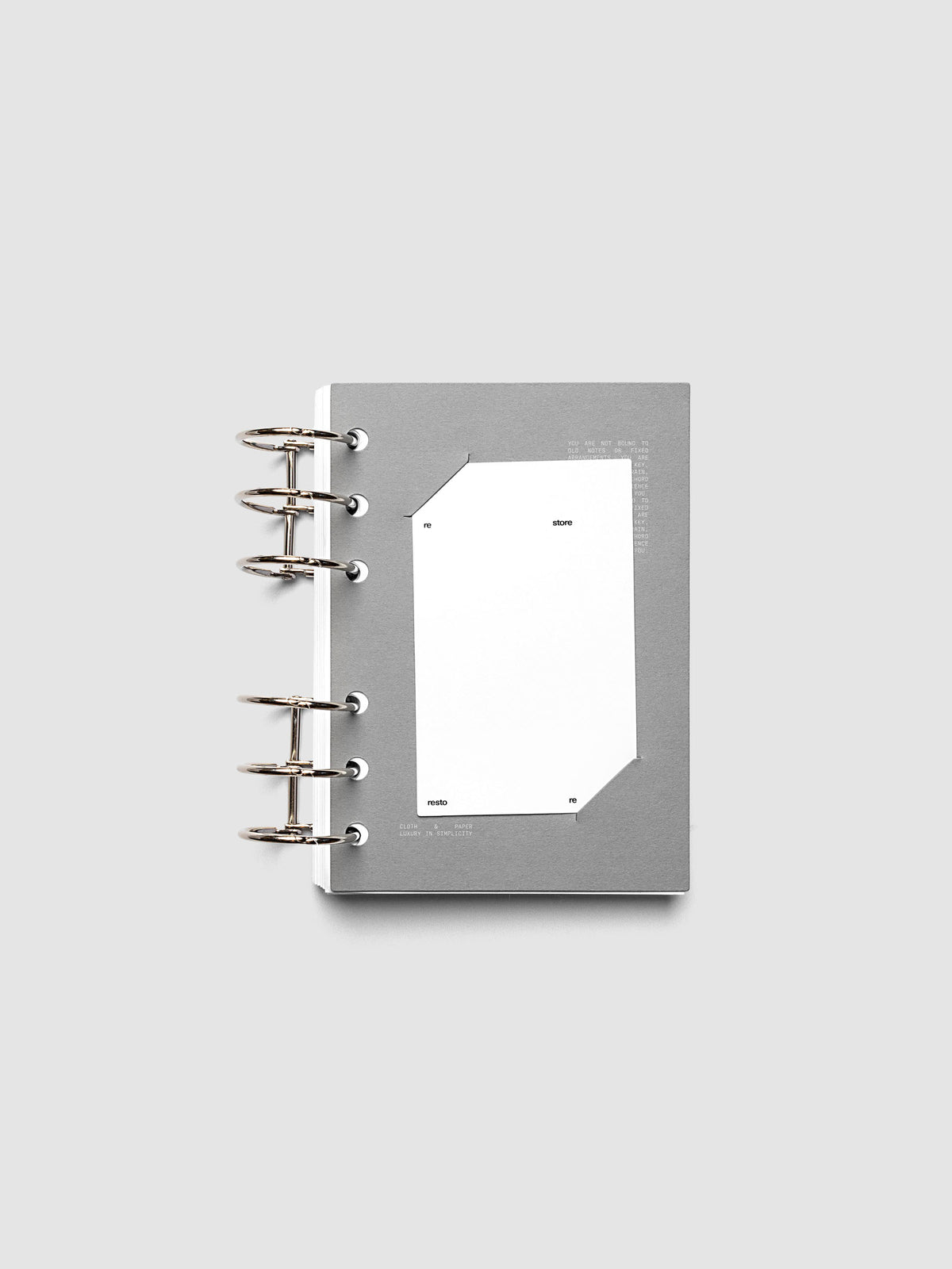 Grey cardstock planner dashboard with white plastic card inserted in slits with white printed text shown in size A6 shown in a ring bound planner.