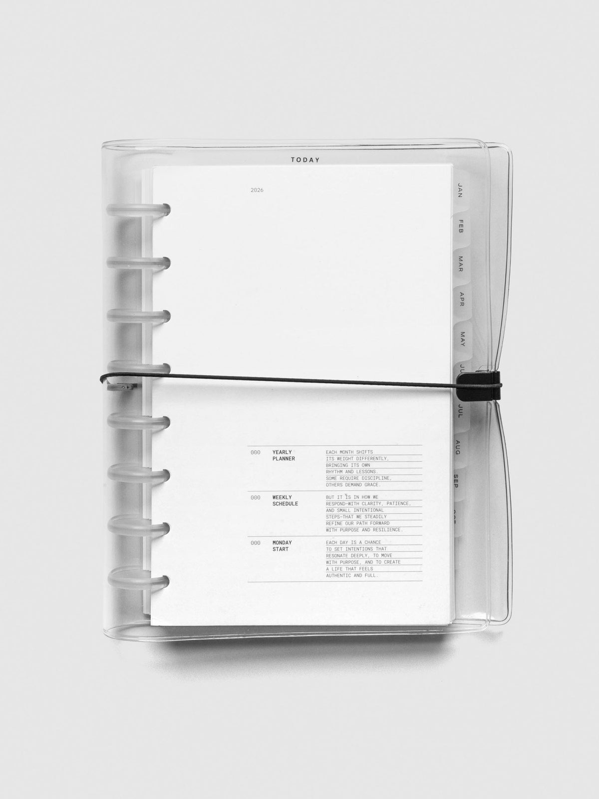 Top-down view of the Half Letter planner with frosted plastic cover and translucent discs. The cover is secured with an elastic band, and the interior page displays the 2026 title and introduction.