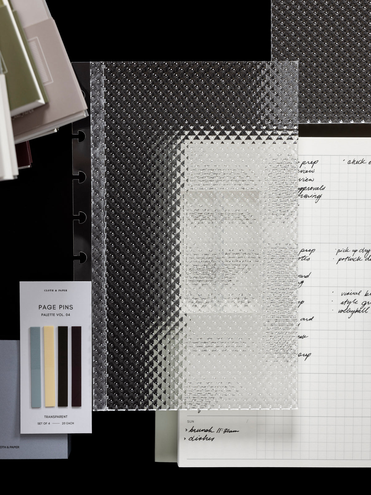Clear, transparent, textured Studded Planner Dashboard shown in size Half Letter in front of a variety of products on a dark background.