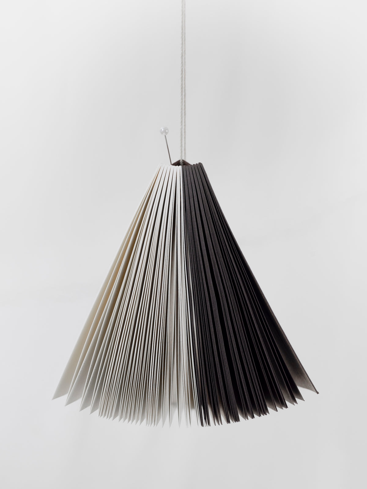 The Common Thread Notebook hanging from a string showing both the brown and white sides of the notebook from the bottom.