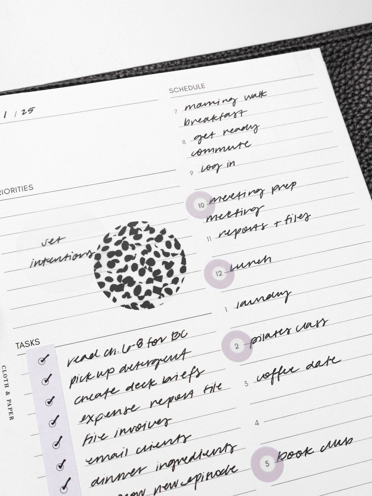 Closeup of inserts in use inside a leather planner. They are filled out with sample text and have been decorated with Spotlight stickers, Strips planner stickers, and a transparent Circle Page Flag.