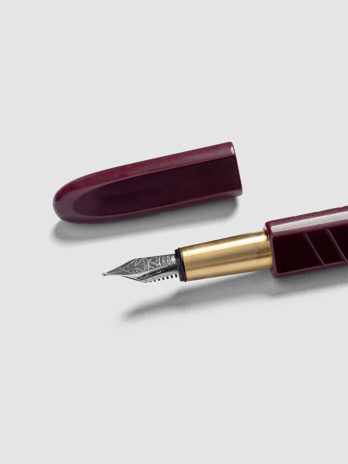 Kolo Tino Fountain Pen in the color Acrylic Cabaret, a deep burgundy barrel with brass accents and a silver medium nib shown with cap off.