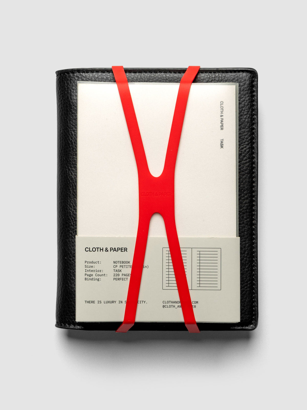 Small, red planner closure band shown holding a CP Petite perfect bound notebook on a CP Petite leather planner cover.