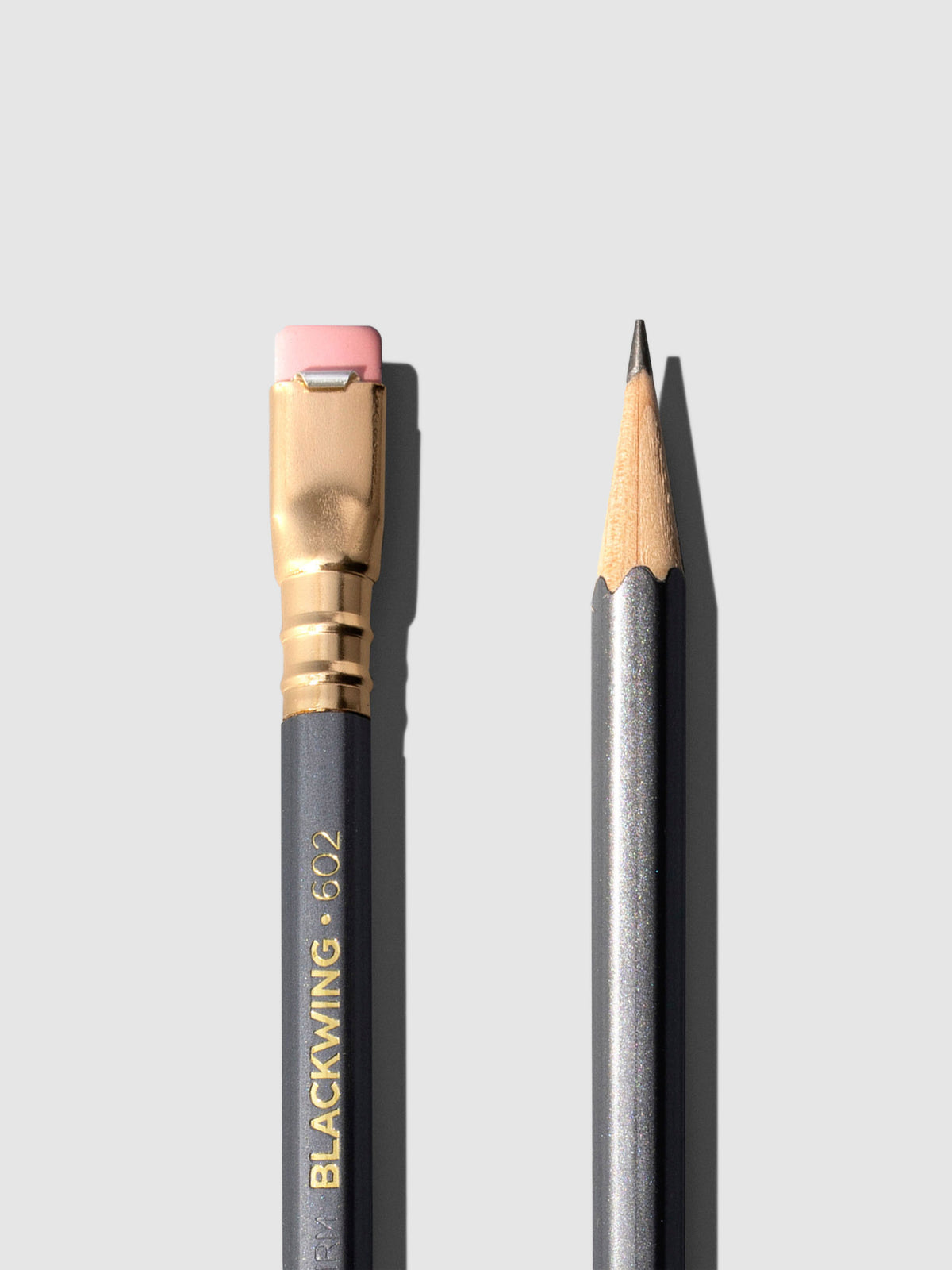 Closeup of two gray wooden pencils displayed on a neutral background. One is shown eraser side up, the other point side up.