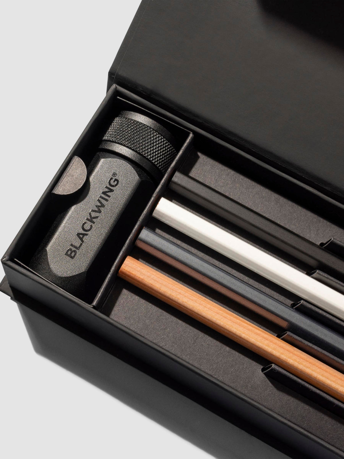 Closeup of four pencils and black pencil sharpener inside black storage box.
