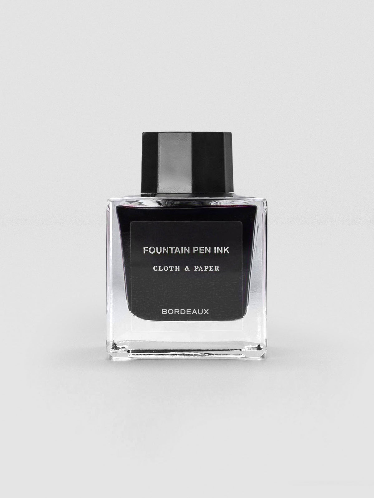 A square glass bottle of Cloth & Paper Fountain Pen Ink in Bordeaux, sealed with a black cap.