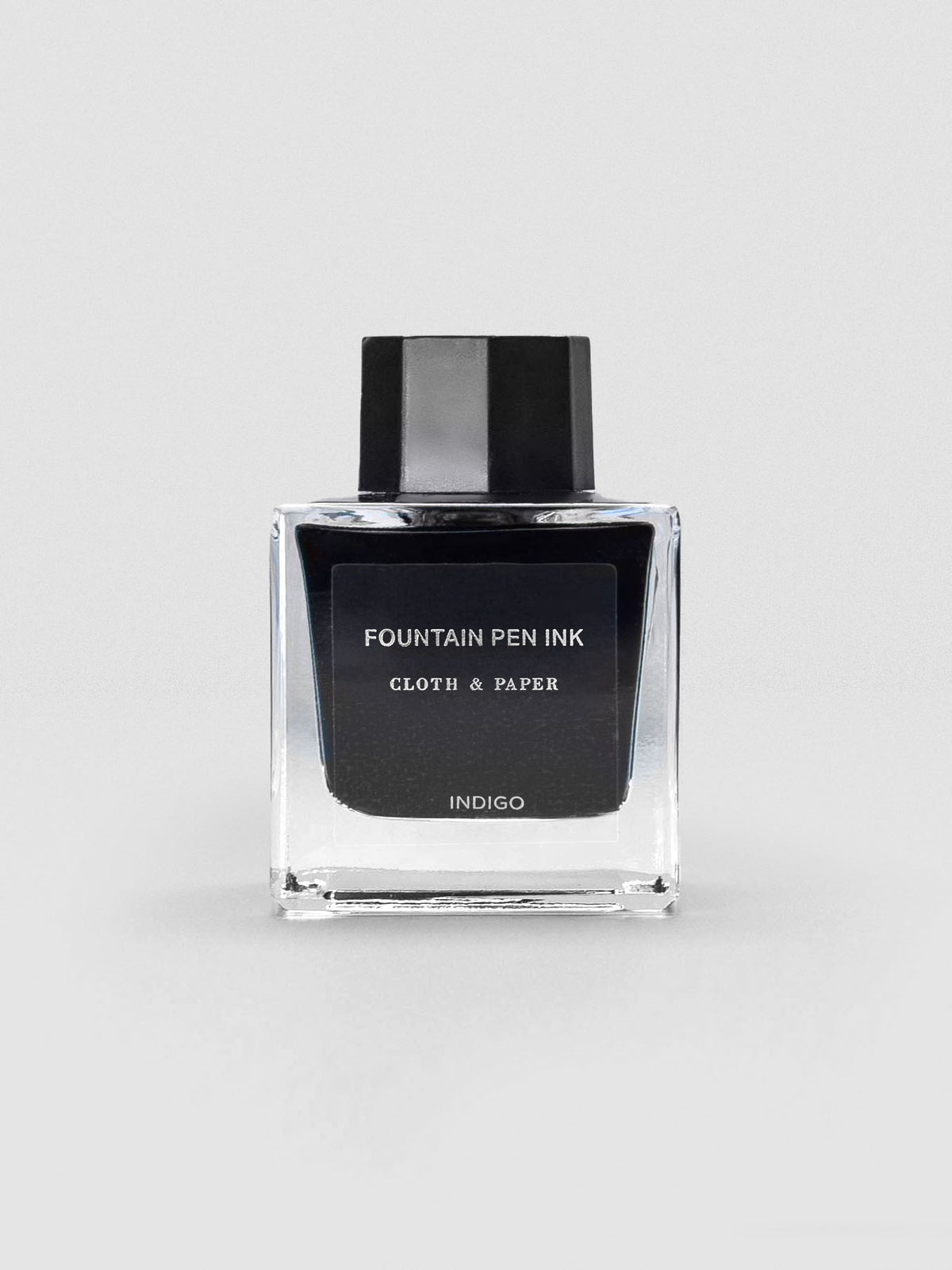 A square glass bottle of Cloth & Paper Fountain Pen Ink in Indigo, shown with a black label and matching black cap.
