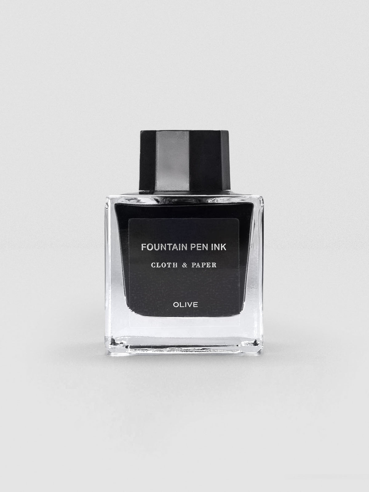 A square glass bottle of Cloth & Paper Fountain Pen Ink in Olive, displayed with a sleek black label and black cap.