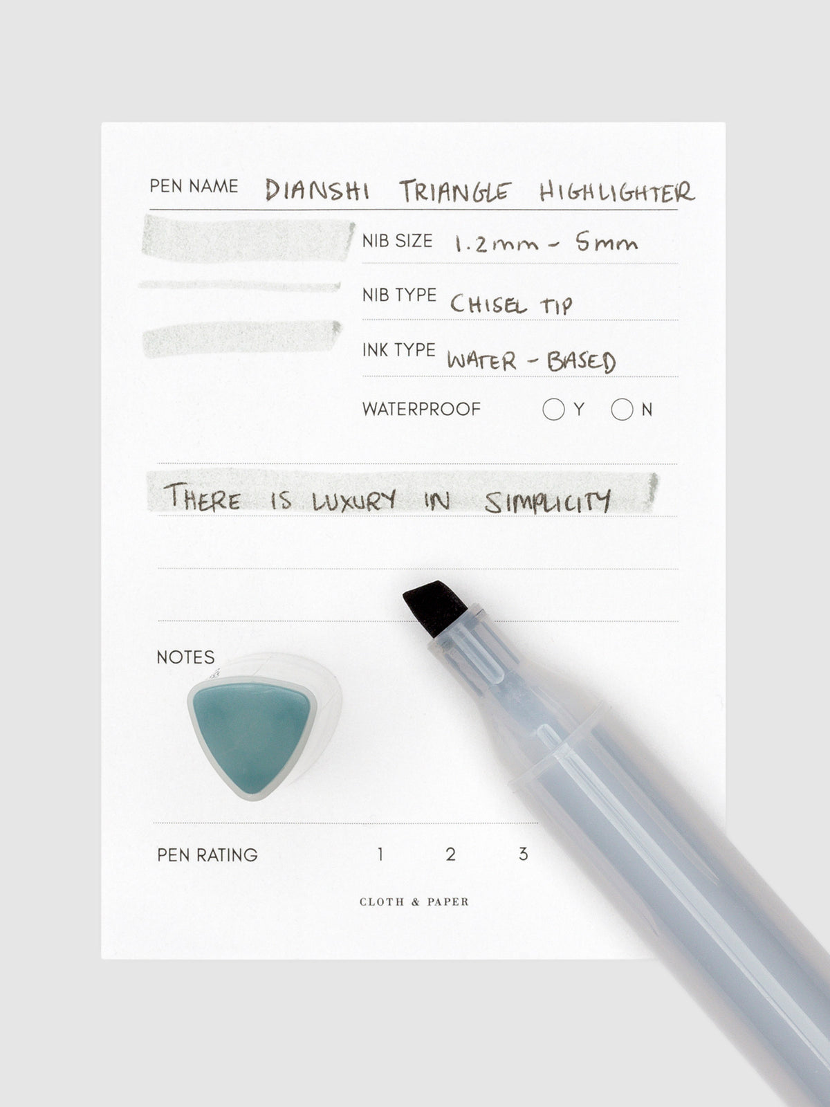 Silver blue highlighter uncapped, resting on a pen test sheet displaying a writing sample detailing the highlighter's specs. The cap stands upright on the bottom left corner of the pen test sheet.