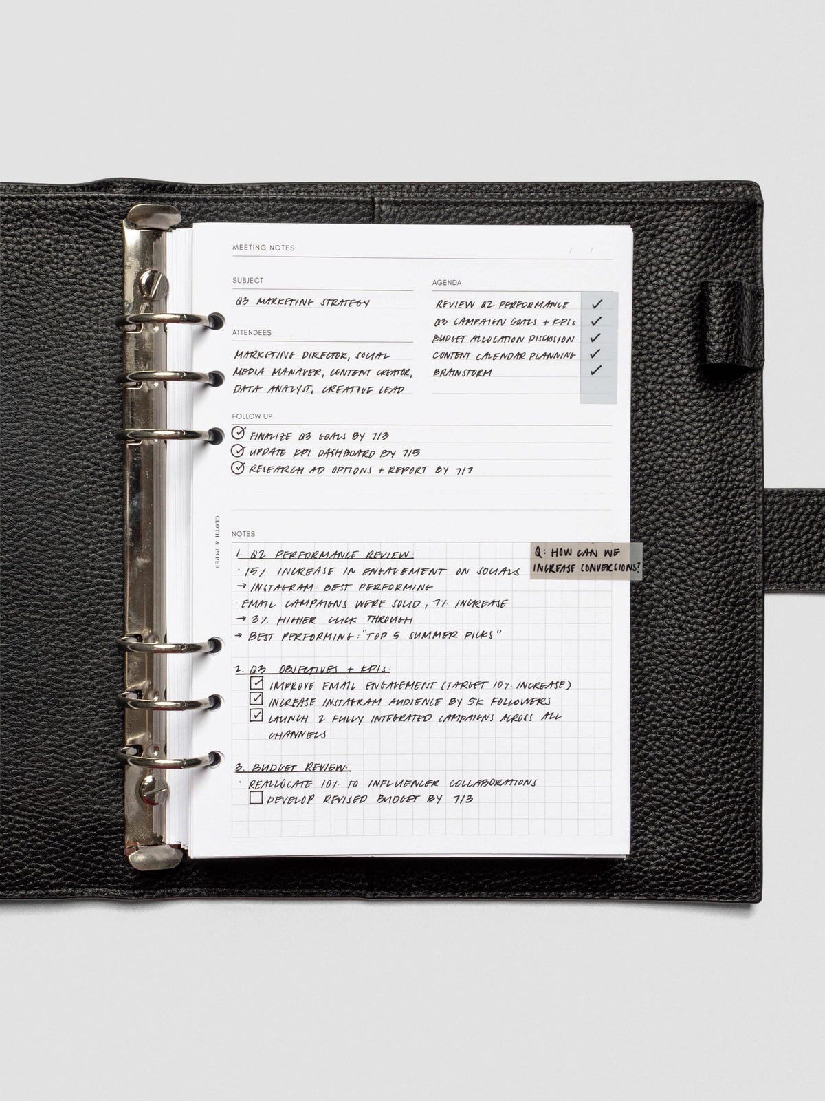 A meeting notes insert neatly filled with handwritten notes, secured in a black leather six-ring planner. The structured layout includes subject, agenda, attendees, follow-up, and a gridded notes section.