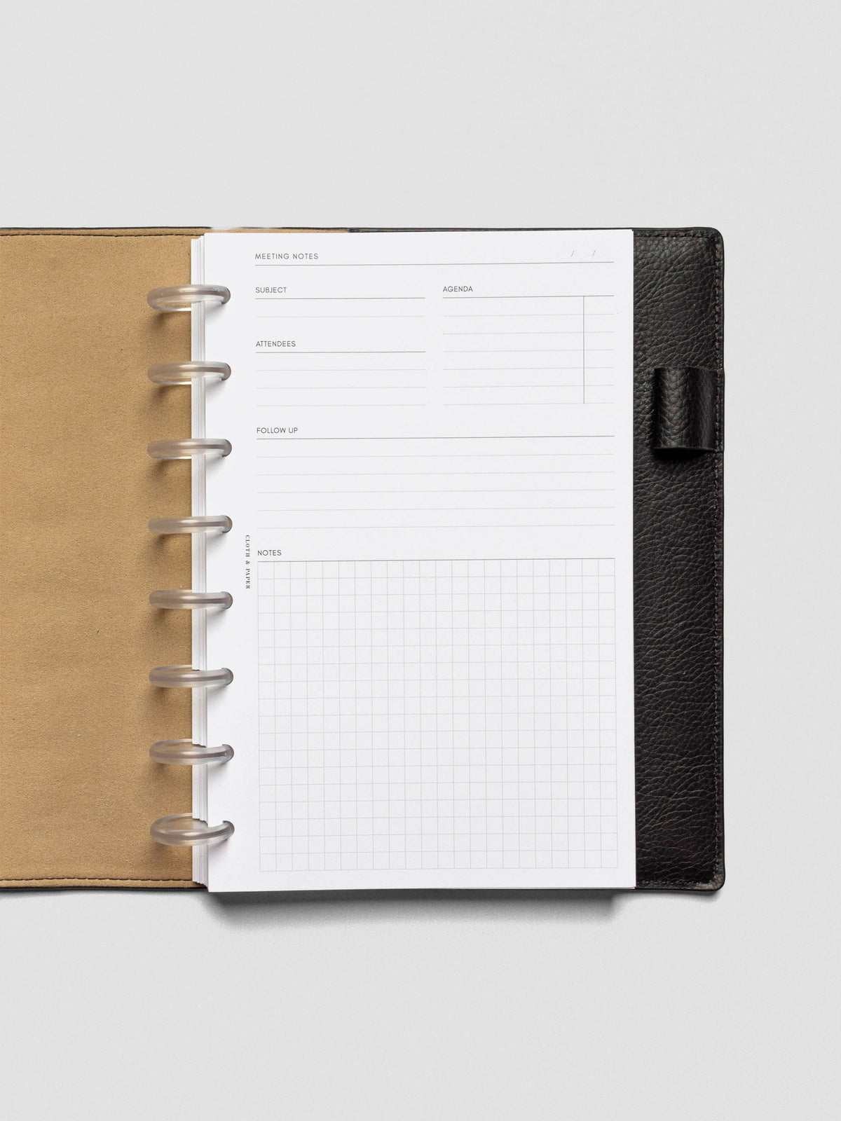 Meeting notes insert displayed in a black leather planner with tan interior. The minimal layout features sections for subject, agenda, attendees, follow-up, and a gridded notes area.