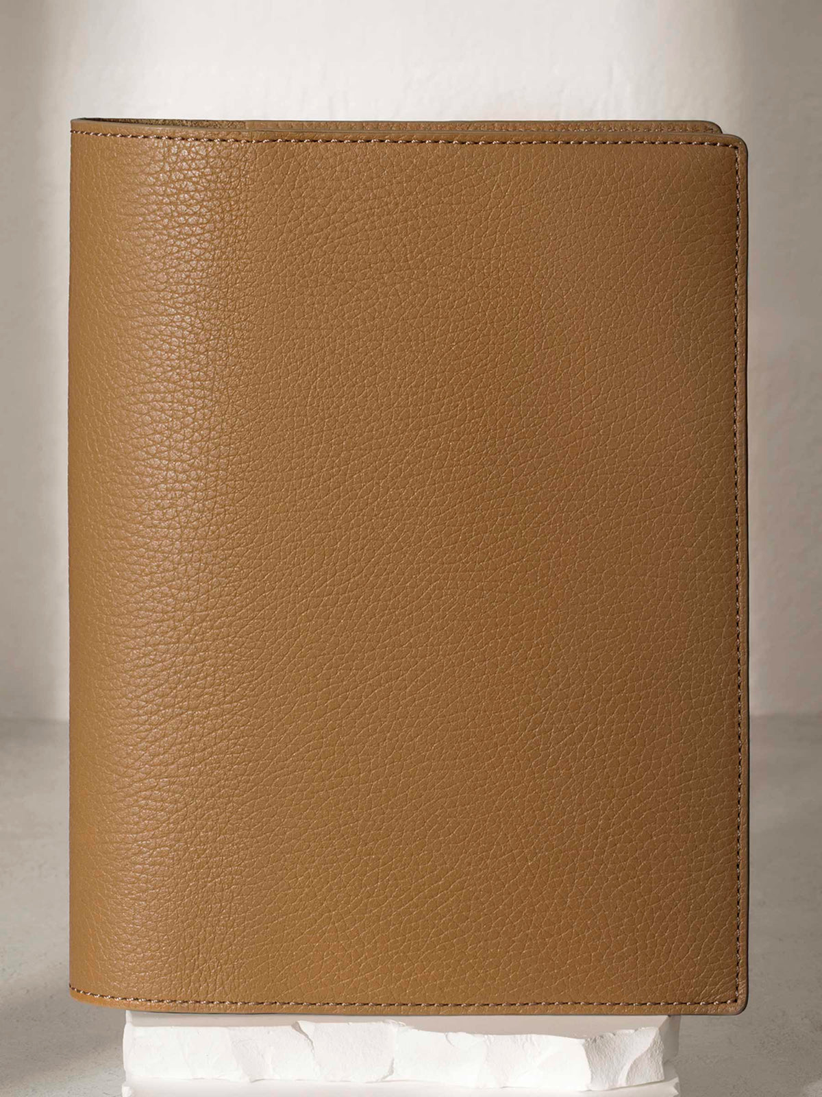 Large Catalonia folio displayed on a white stone pedestal. The background is a natural textured off-white material, and a spotlight behind the folio highlights its placement.
