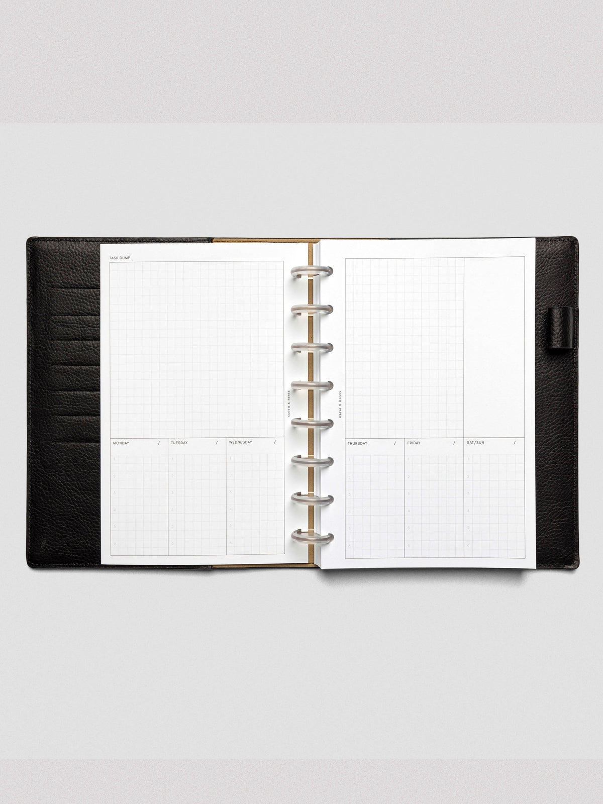 A weekly planner spread featuring a large "Task Dump" section at the top and segmented days of the week below, with six numbered grid slots for each day. Bound in a black leather discbound planner.
