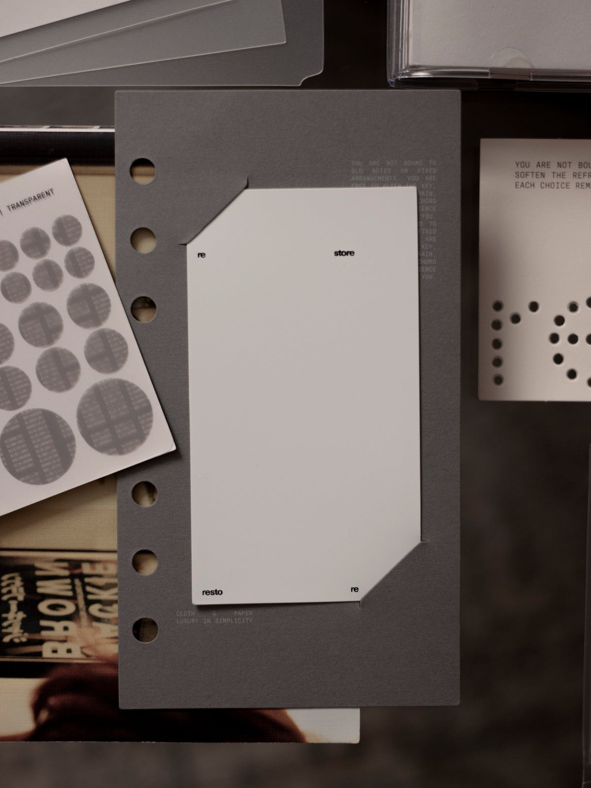 Personal sized grey matte paper dashboard with plastic layer insert into paper slits with other items around it.