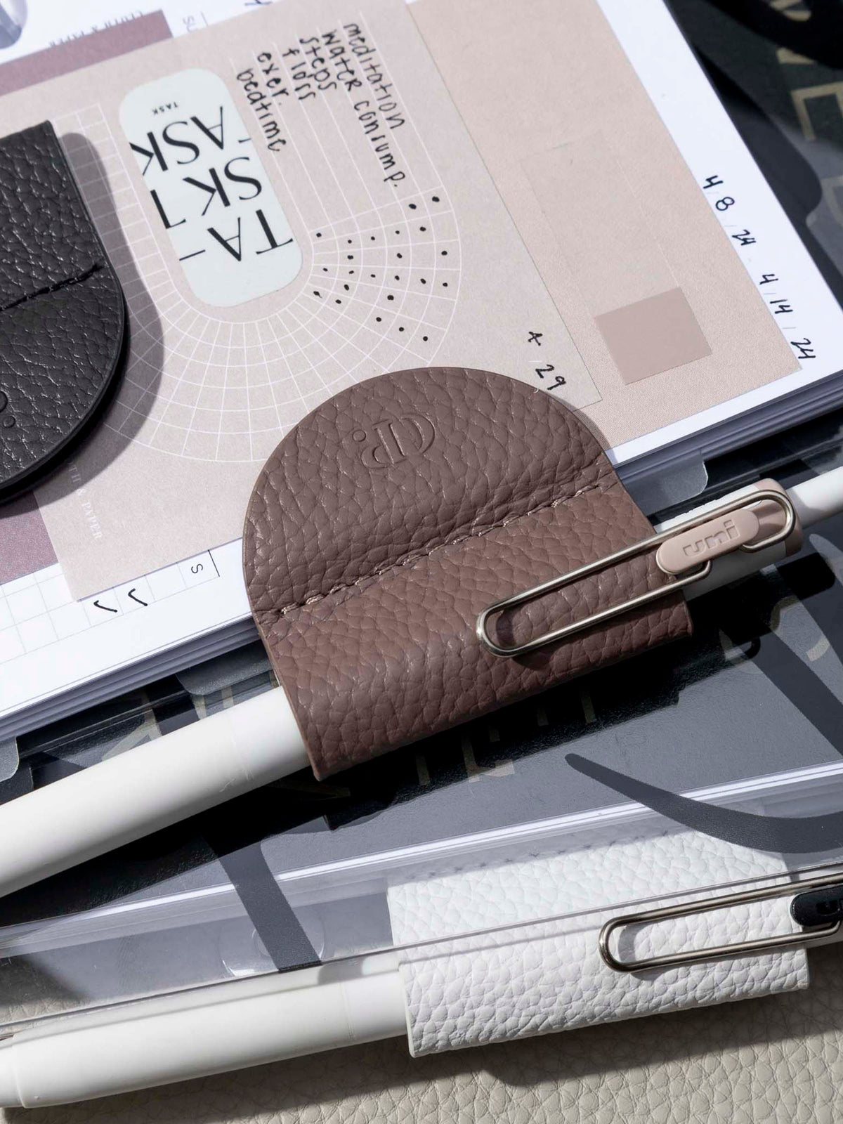 Image shows three variants of the eCLIPse Leather Bookmark Pen Holders used to clip pens onto some planners.