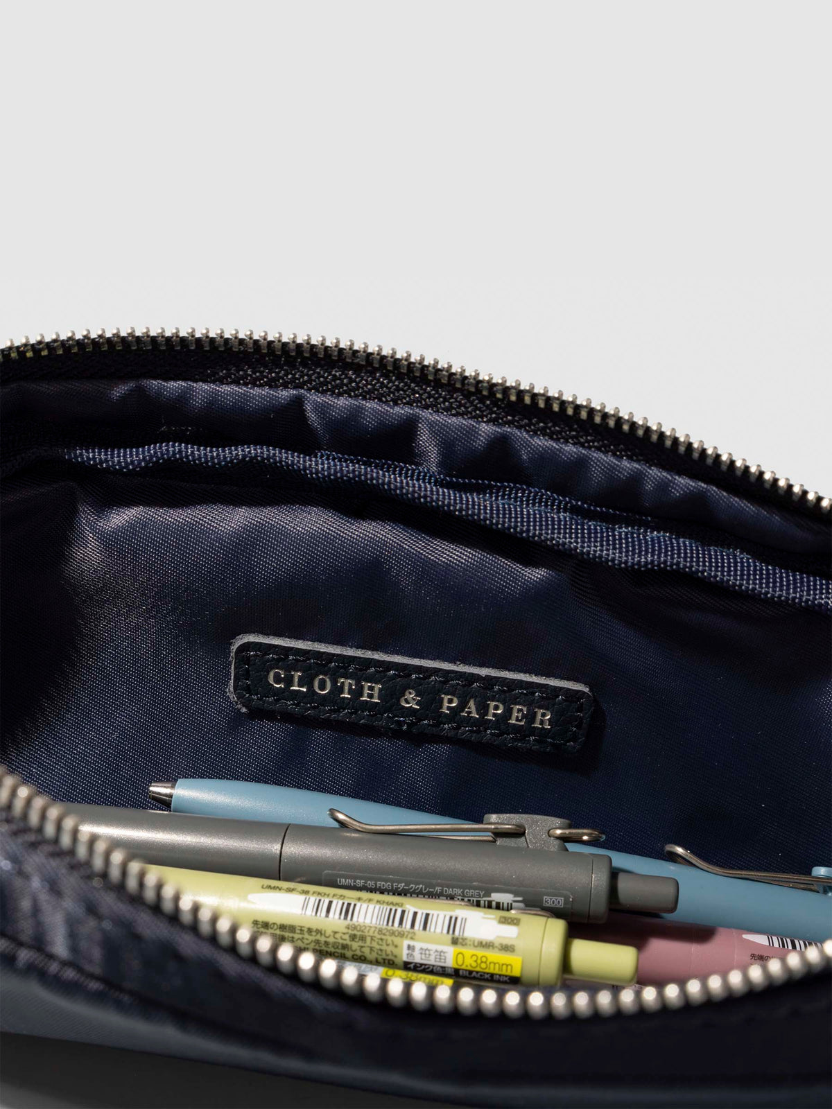 Closeup of Cloth and Paper logo inside of pencil pouch. A selection of pens are stored inside the pouch. Color featured is Apollo.