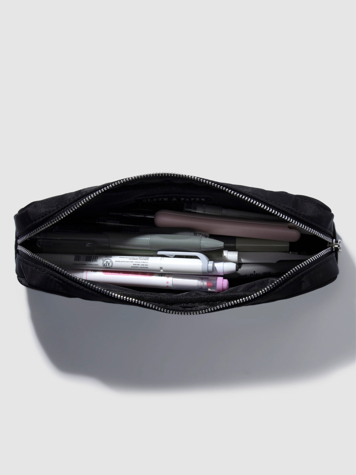 Pencil pouch displayed unzipped with a collection of pens and accessories stored inside. Color featured is black.