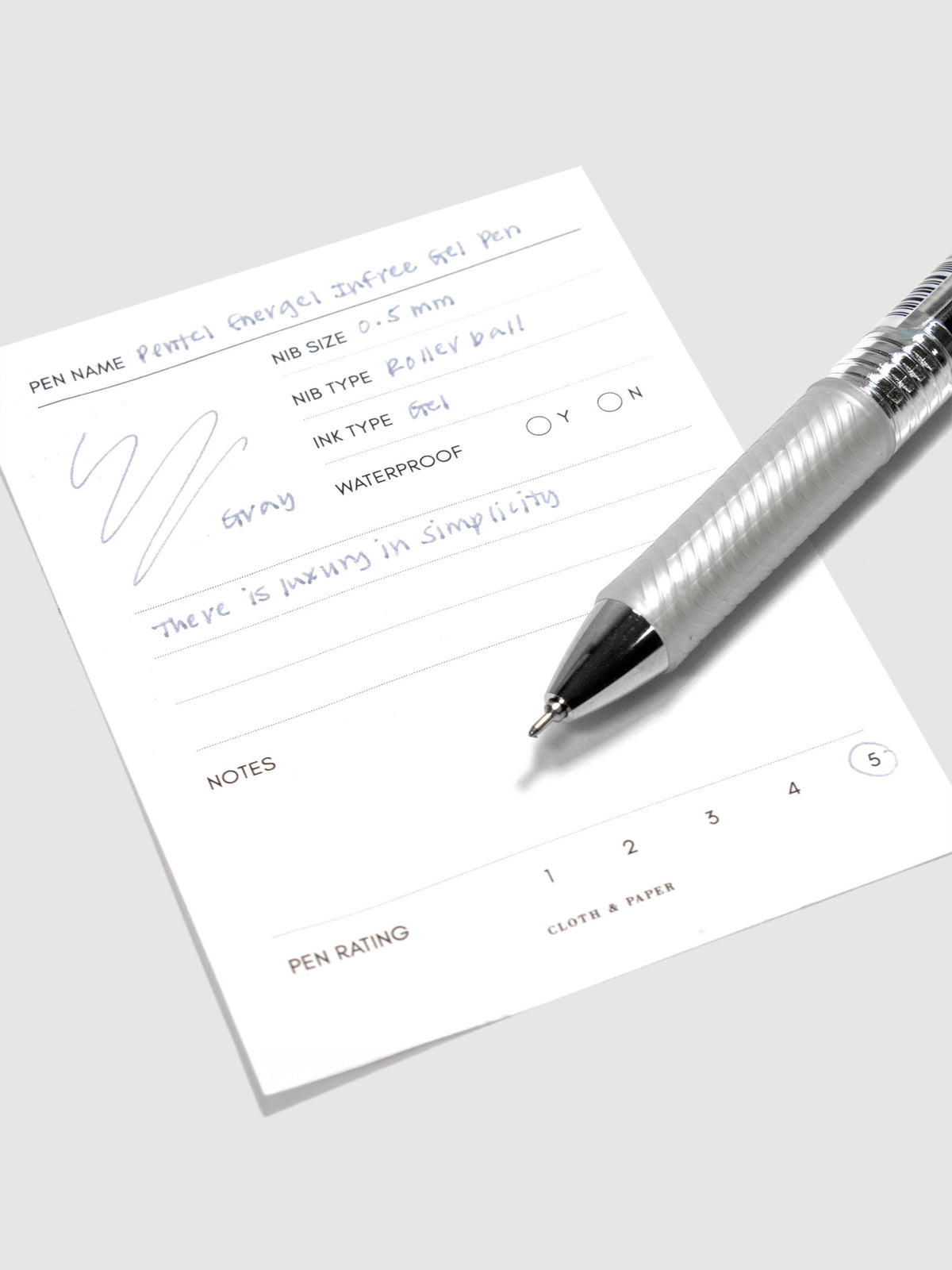 Pentel Energel Infree Gel Pen, Gray, Cloth and Paper. Pen resting on pen test sheet displaying writing sample.