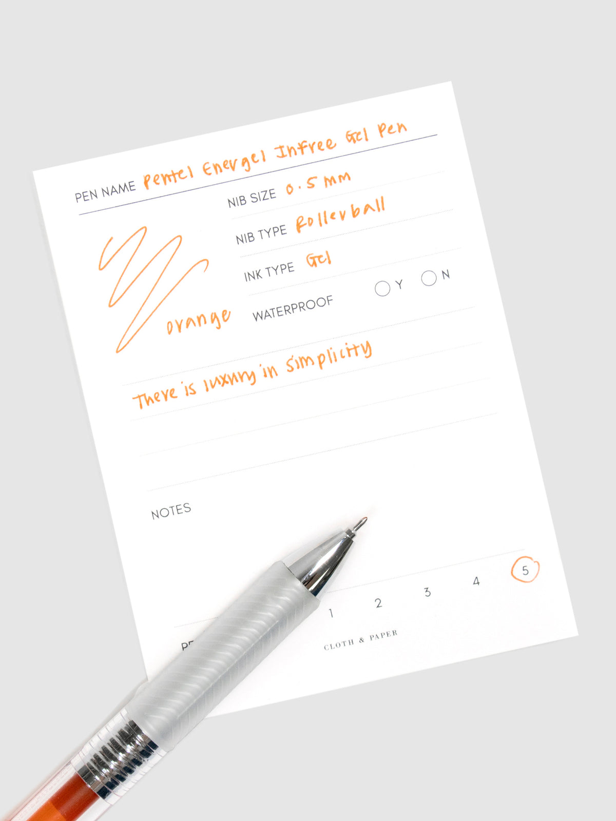 Pentel Energel Infree Gel Pen, Orange, Cloth and Paper. Close up on pen nib resting on pen test sheet.