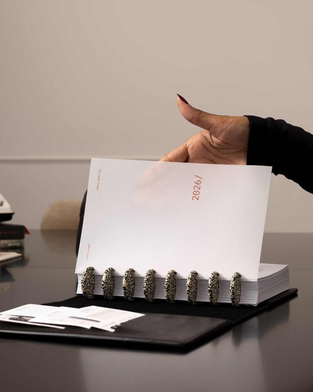 Hand flipping through a planner with bold speckled discs and a 2026 cover page inside a black leather folio.