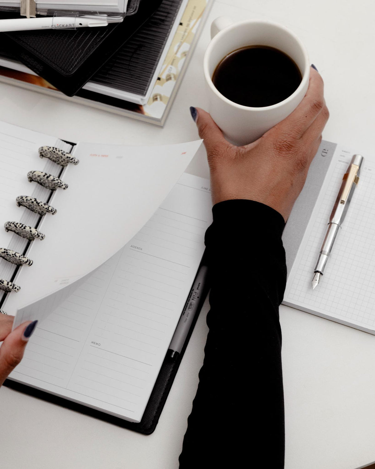 A desk setup with a cup of coffee, grid notepad, and open planner showcasing speckled discs and weekly planning inserts.