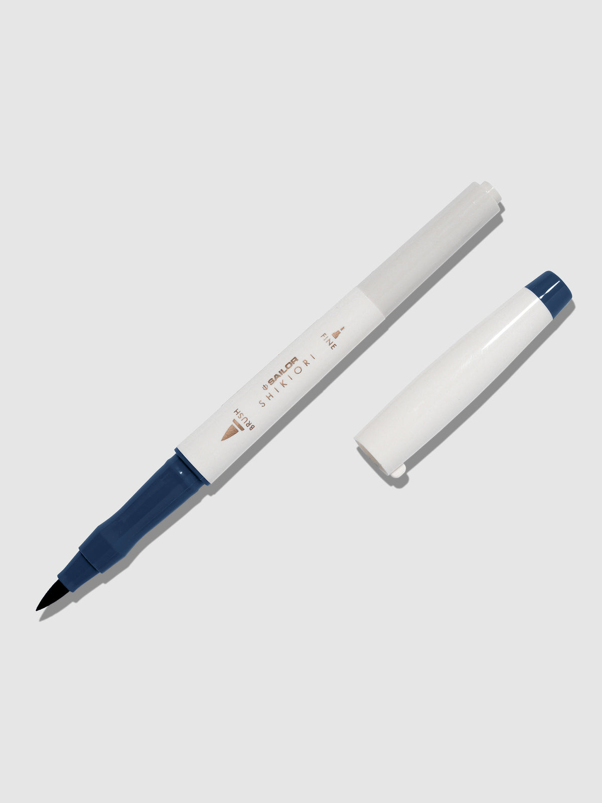 Brush pen displayed on a neutral background. It is uncapped with its brush nib exposed, and the cap lying parallel to the marker. Color pictured is Yonaga.