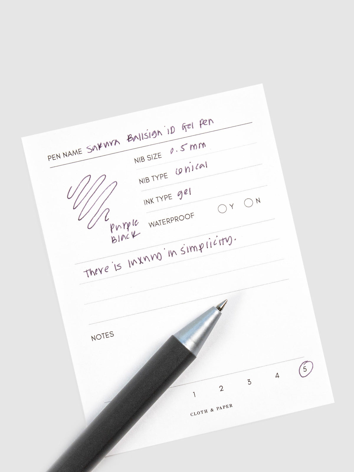 Pen in Purple Black resting on a pen test sheet displaying a writing sample detailing the pen's specs.