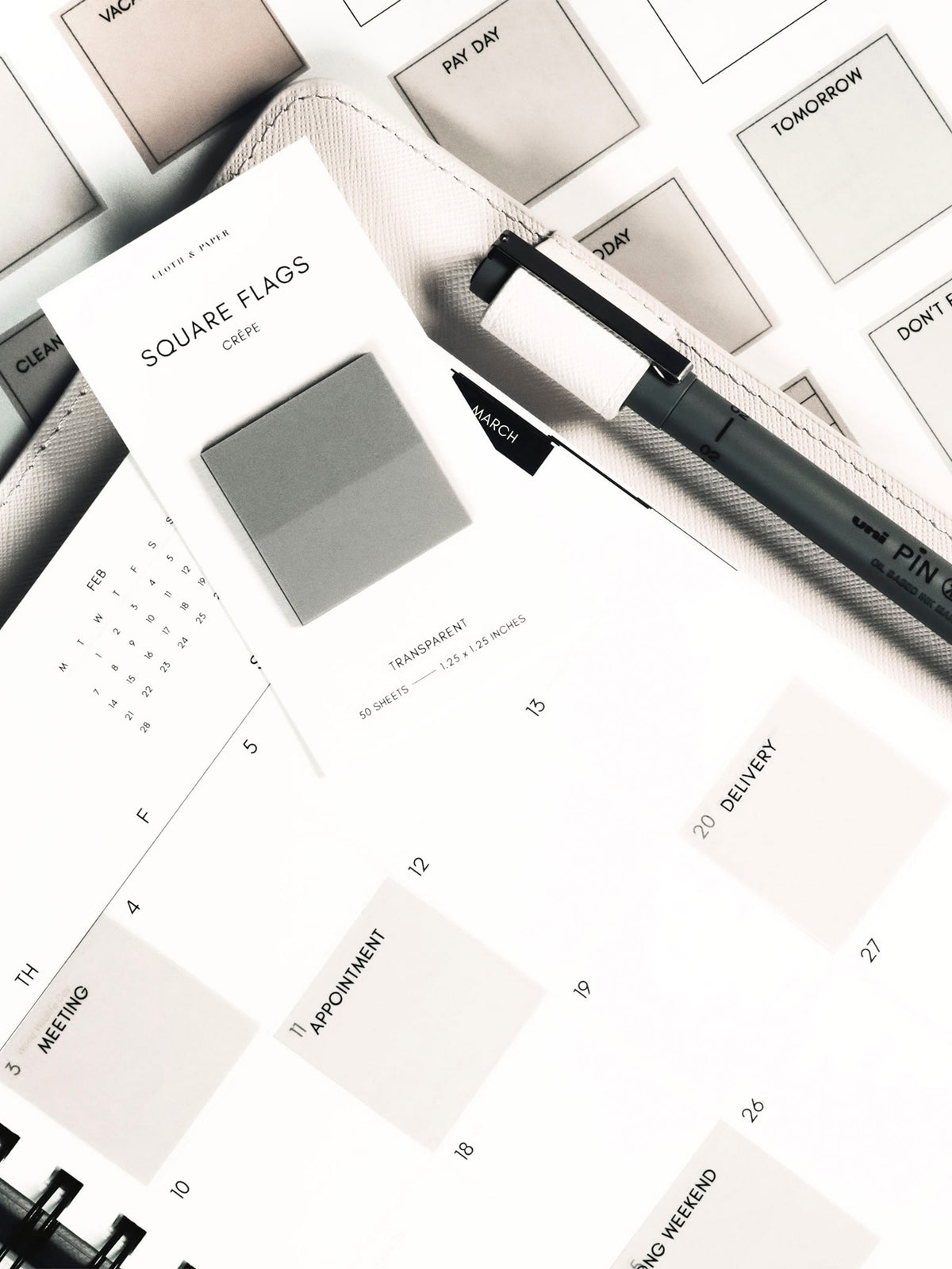 Square Page Flag Printable | Essentials page layered under a planner showing page flags in use. A Uni Pin Marking Pen is in the planner's pen loop and a set of square page flags are resting on top of the planner.
