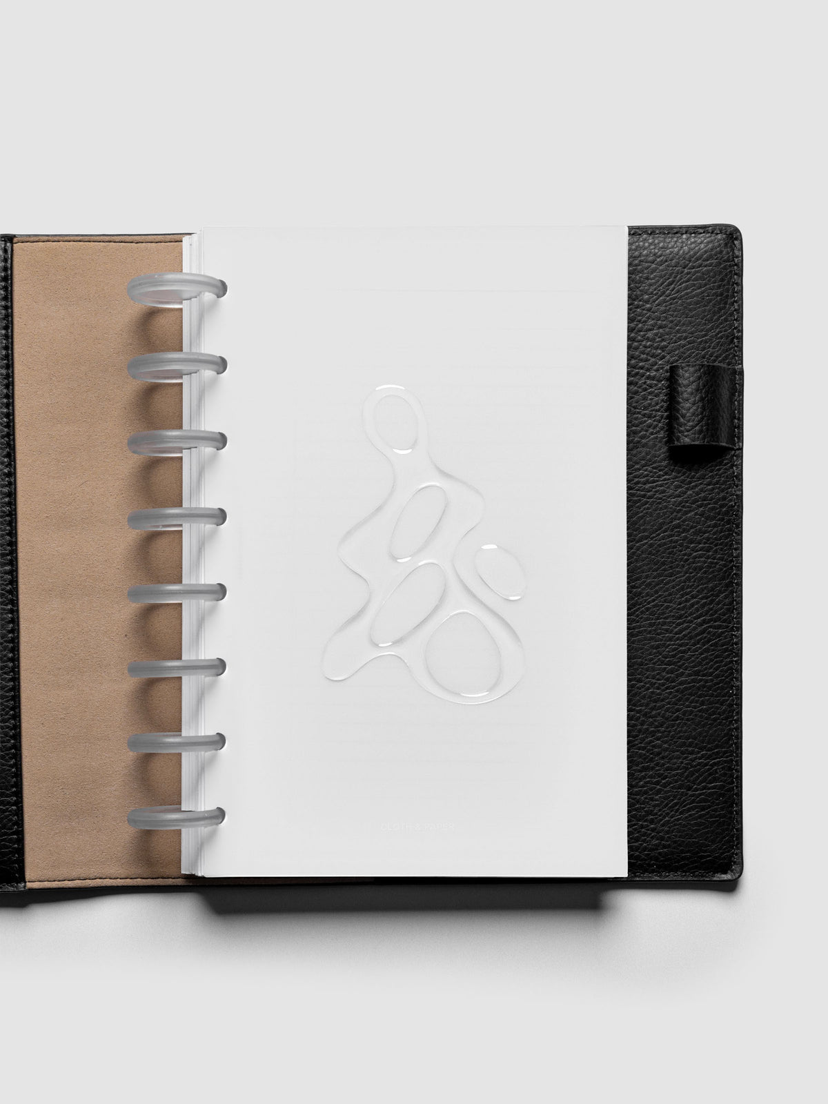 Light grey, semi-transparent, and glossy plastic planner dashboard with organic raised shape design in size Half Letter shown discbound in a black leather folio.