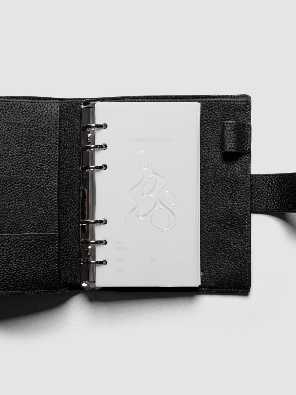 Light grey, semi-transparent, and glossy plastic planner dashboard with organic raised shape design in size Personal shown ringbound in a black leather agenda.