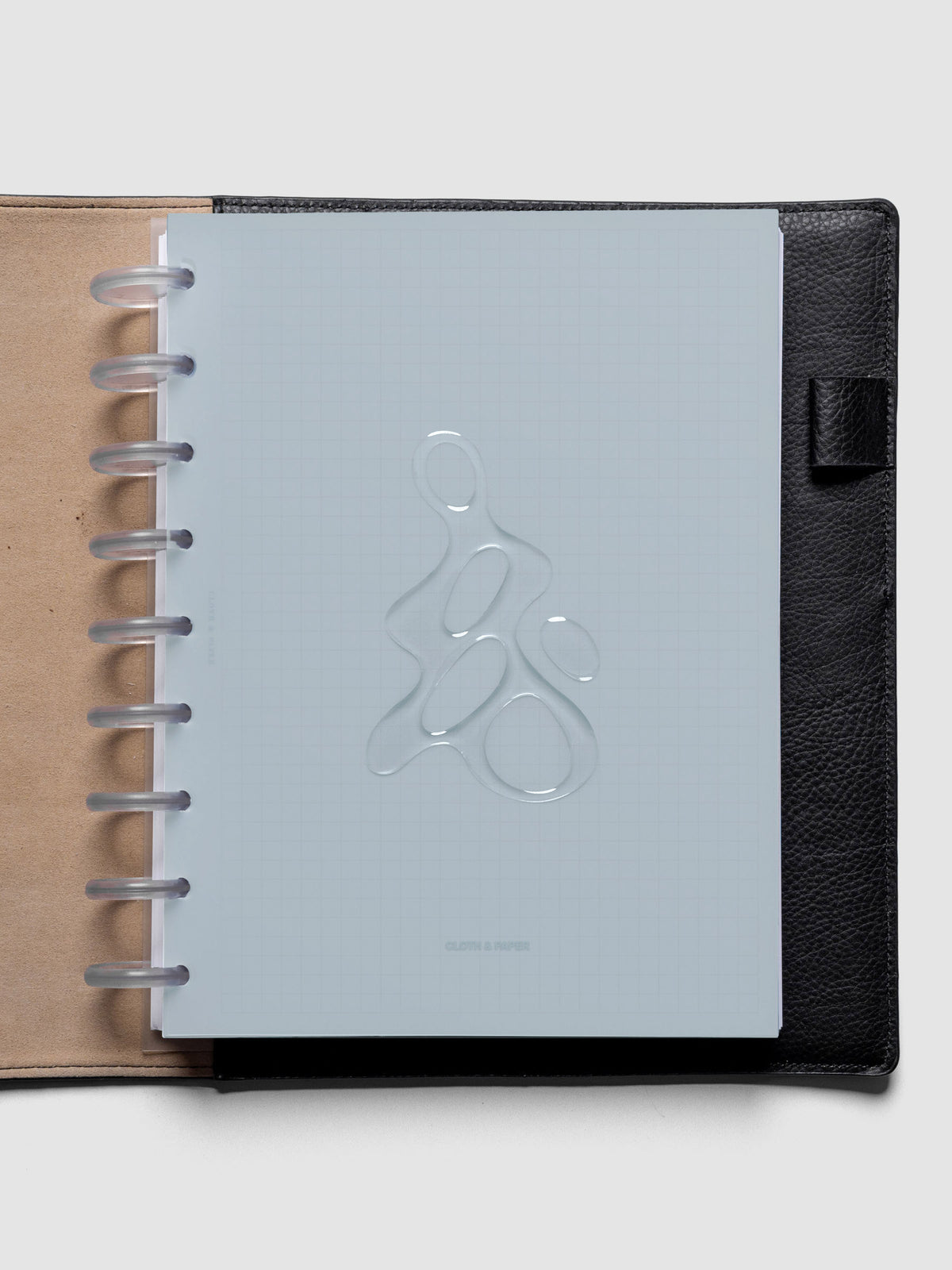 Light blue, semi-transparent, and glossy plastic planner dashboard with organic raised shape design in size HP Classic shown discbound in a black leather folio.