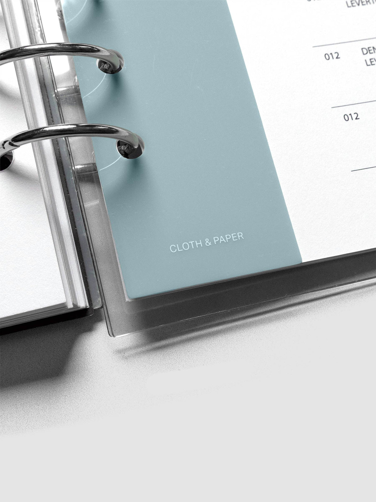Close up of the Cloth & Paper logo on a light blue narrow page marker placed in a planner.