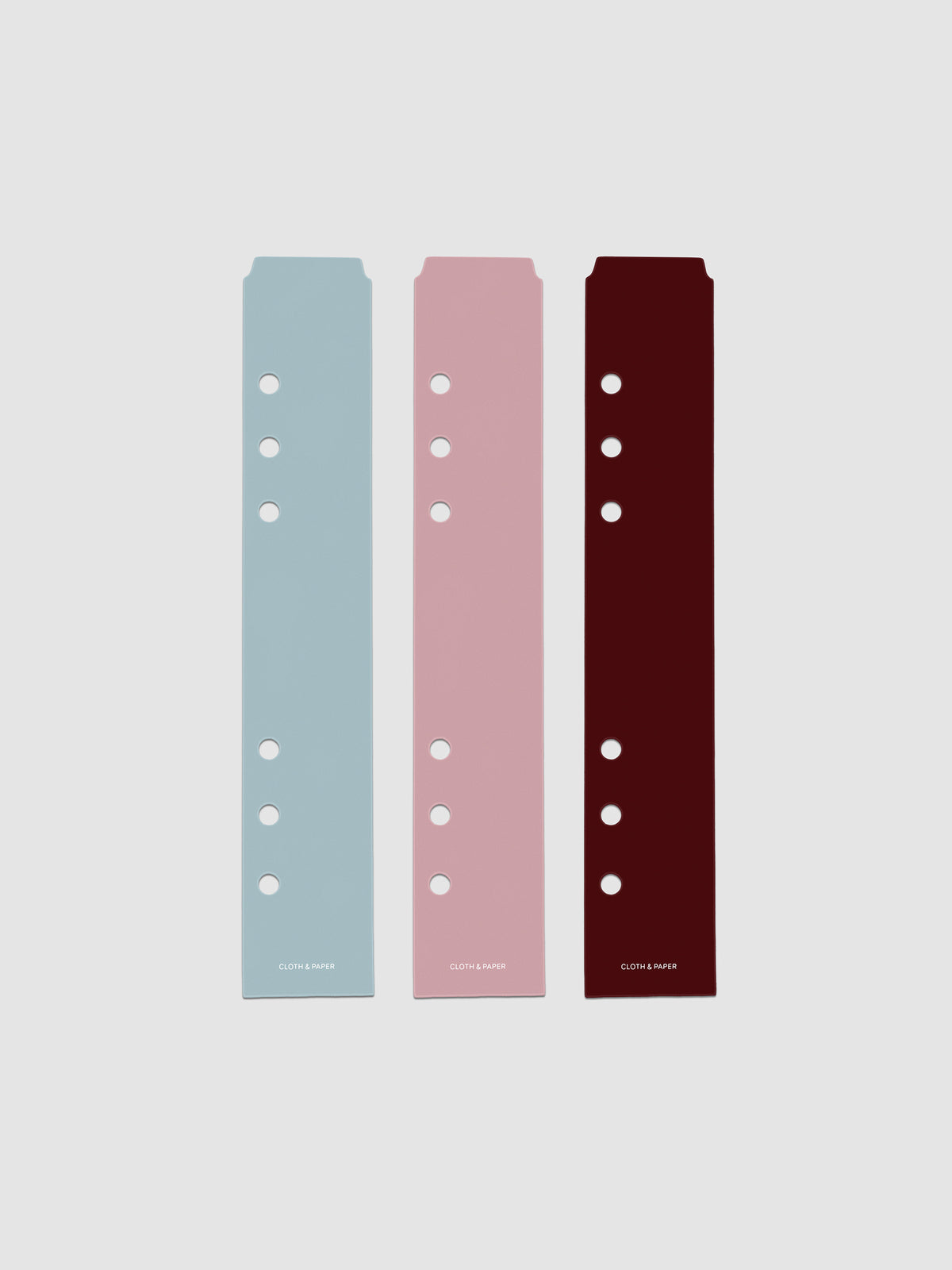 Set of three narrow page markers pre-punched for A5 planners in light blue, pink, and burgundy on a neutral background.
