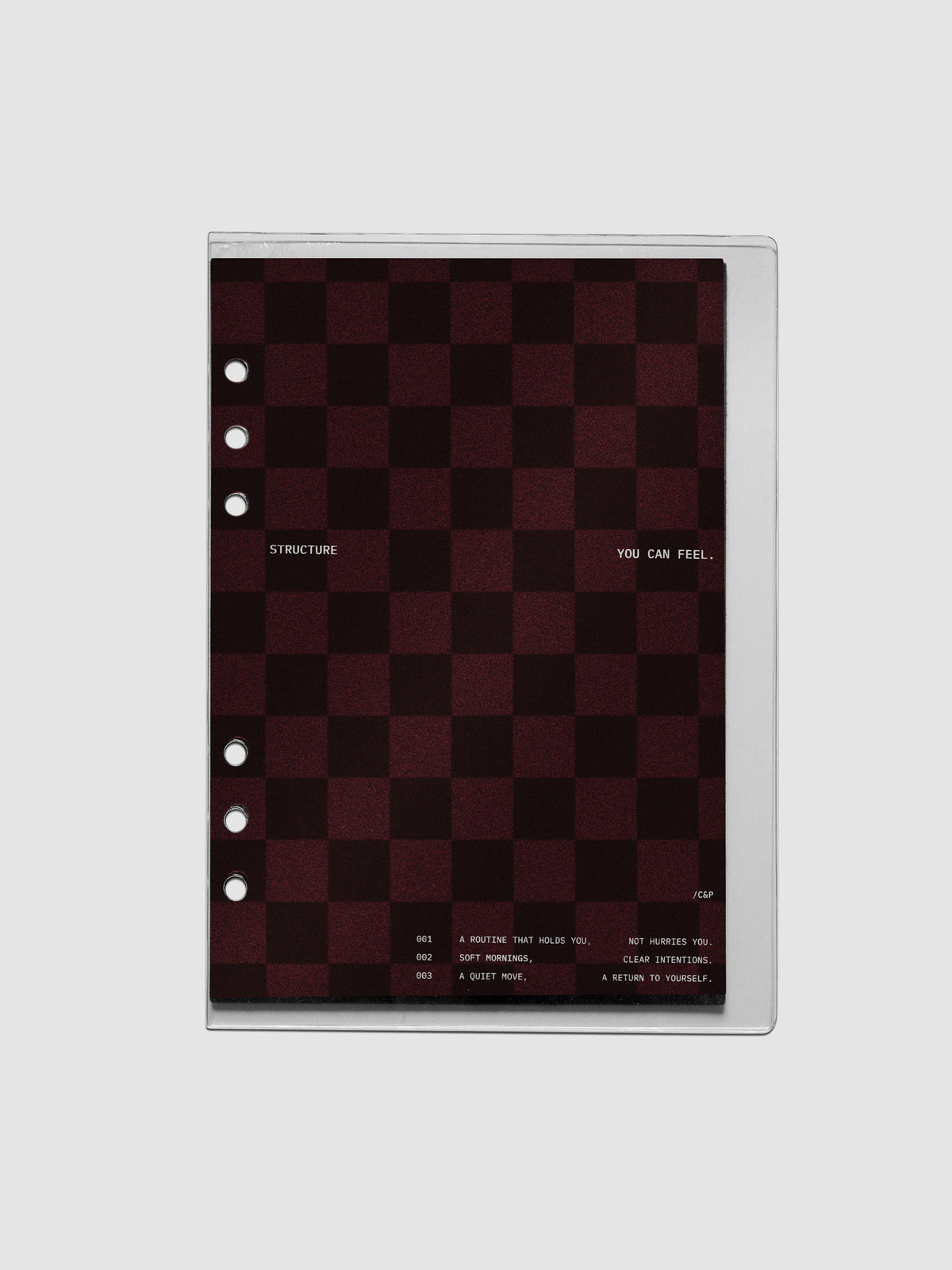 A5 sized velvet checkered dashboard in the color Bordeaux in between two crystal clear plastic planner covers with text printed on the cover on the theme of structure and routines.