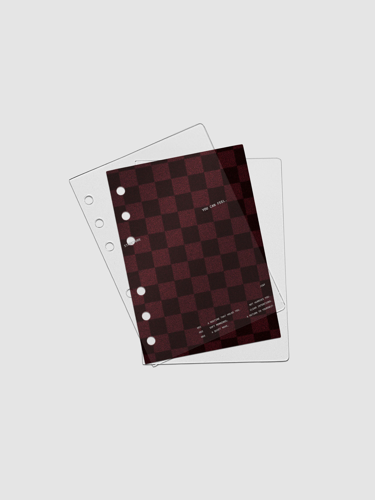 A6 sized velvet checkered dashboard in the color Bordeaux in between two crystal clear plastic planner covers with text printed on the cover on the theme of structure and routines.