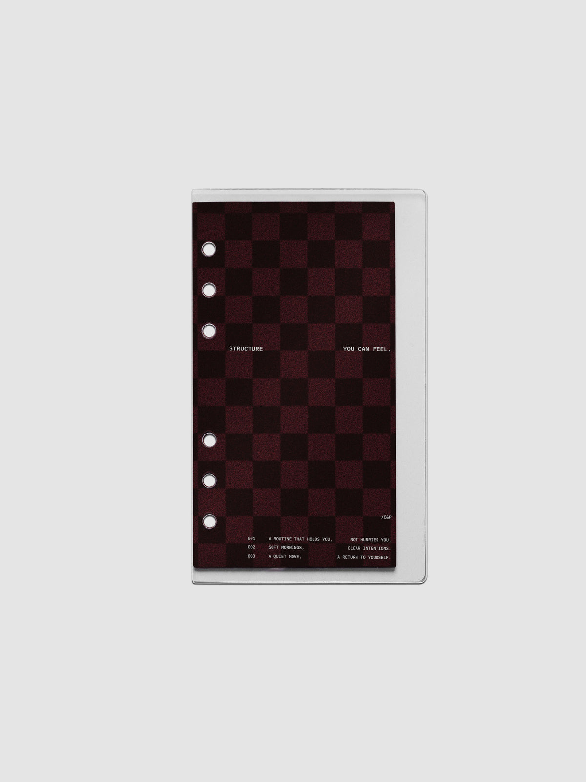 Personal sized velvet checkered dashboard in the color Bordeaux in between two crystal clear plastic planner covers with text printed on the cover on the theme of structure and routines.