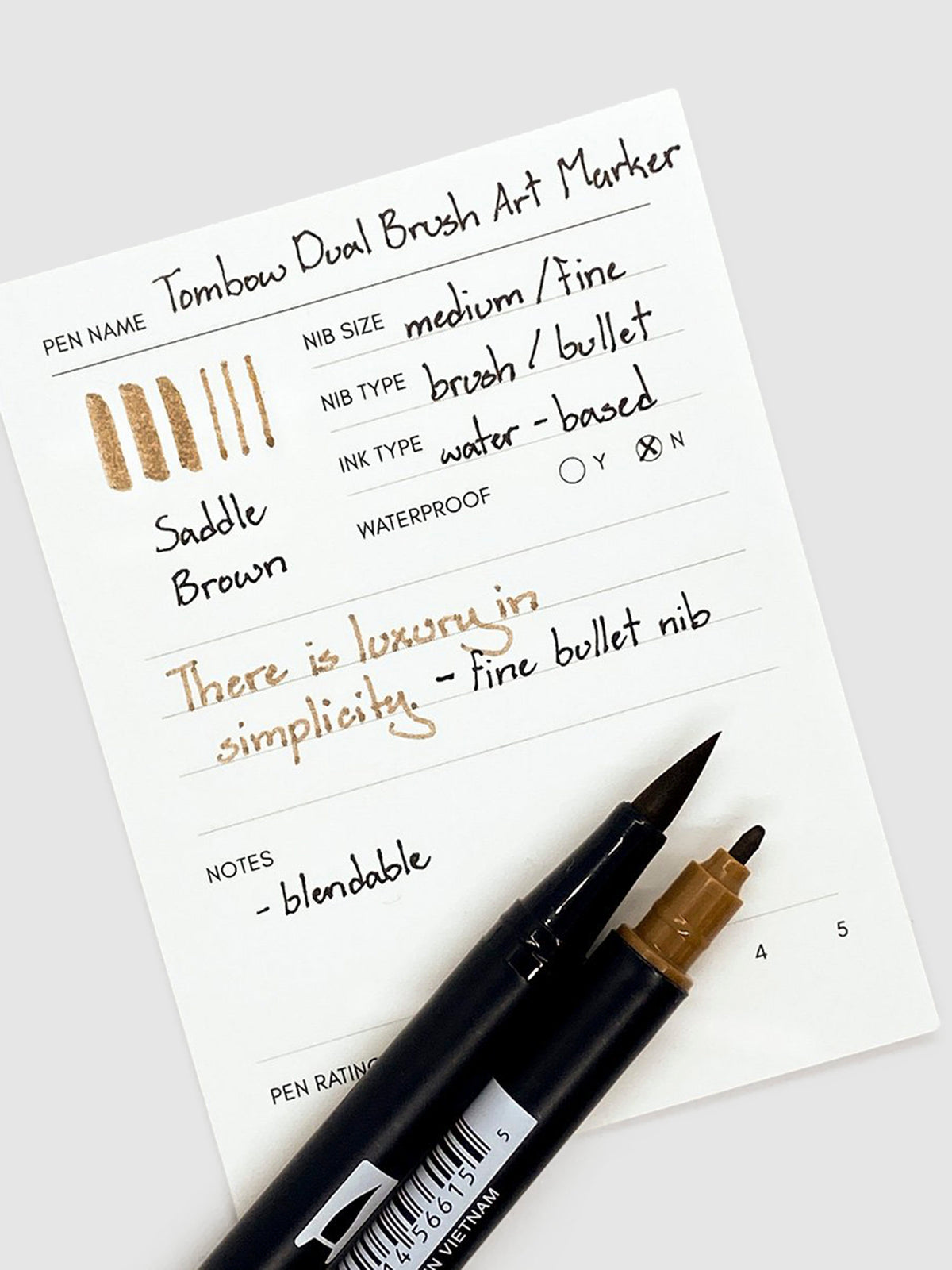 Tombow Dual Brush Art Marker, Saddle Brown, Cloth & Paper. Two Saddle Brown art markers rest with their tips exposed on a pen test sheet.