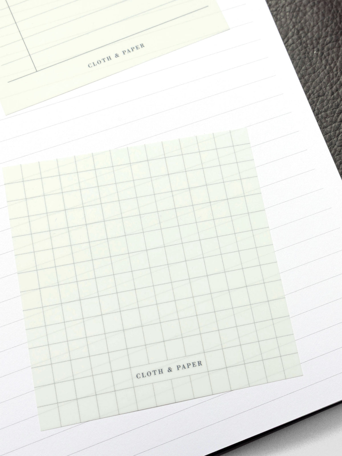 A transparent graph sticky note placed on lined planner paper, showing the grid pattern clearly while still allowing the lines beneath to be visible.