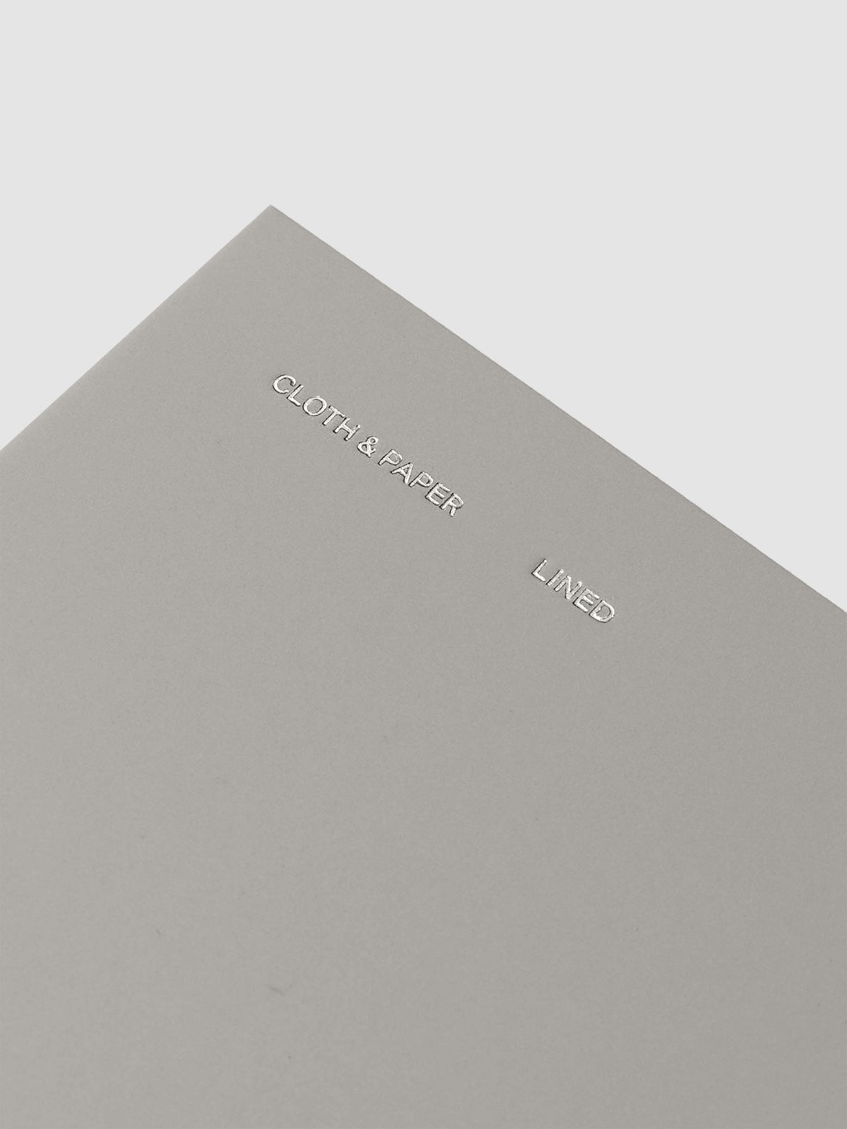 Travel Notebook in size Pocket Plus in the color Ash (grey) containing lined notes layouts shown closed from the front as a closeup on the foil details reading 'Cloth & Paper' 'Lined'.