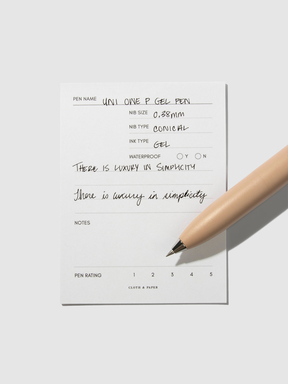Uni-Ball One P pen resting on a pen test sheet. The sheet shows the pens specs. Color pictured is Coffee.