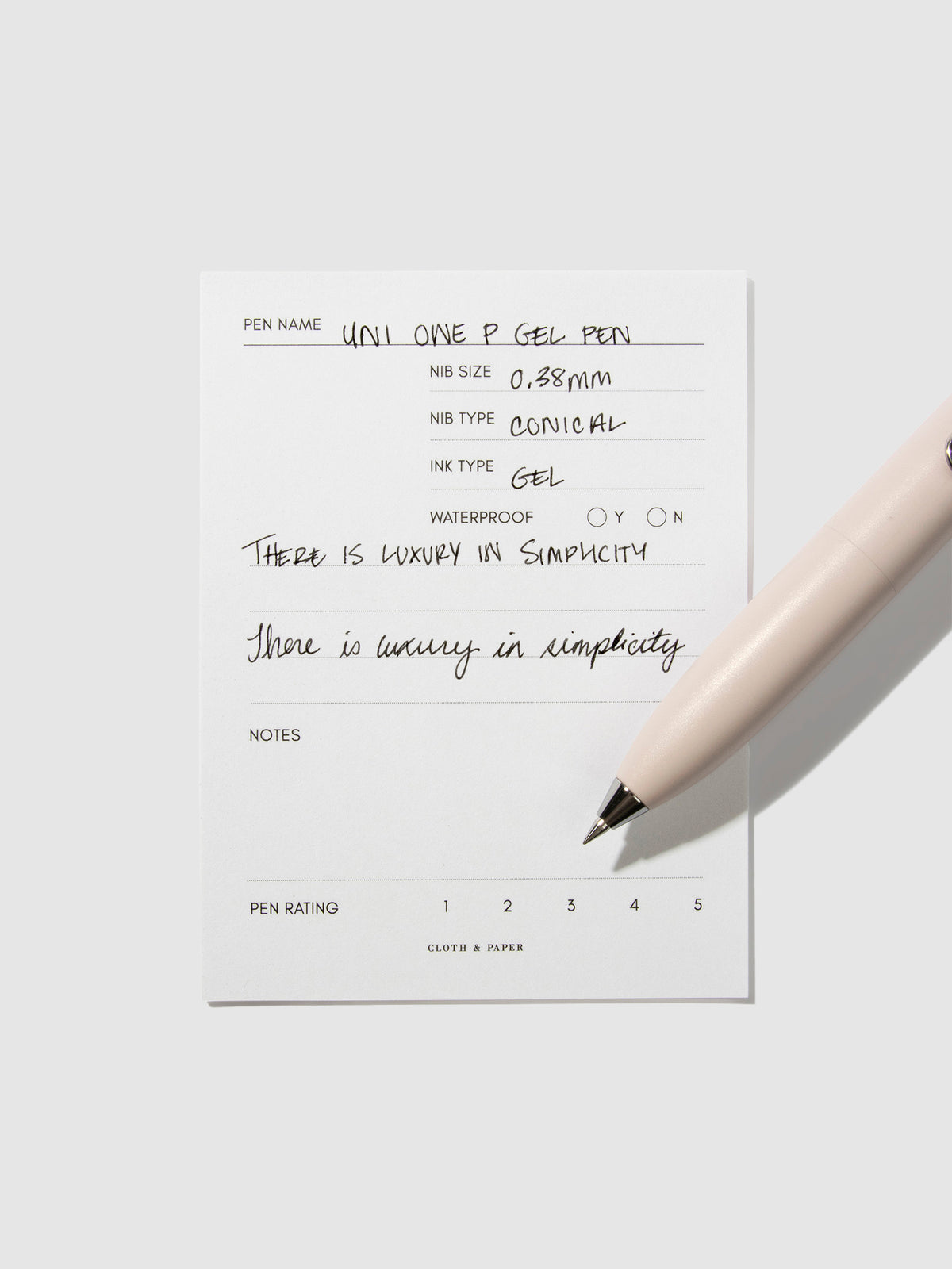 Uni-Ball One P pen resting on a pen test sheet. The sheet shows the pens specs. Color pictured is Peach.