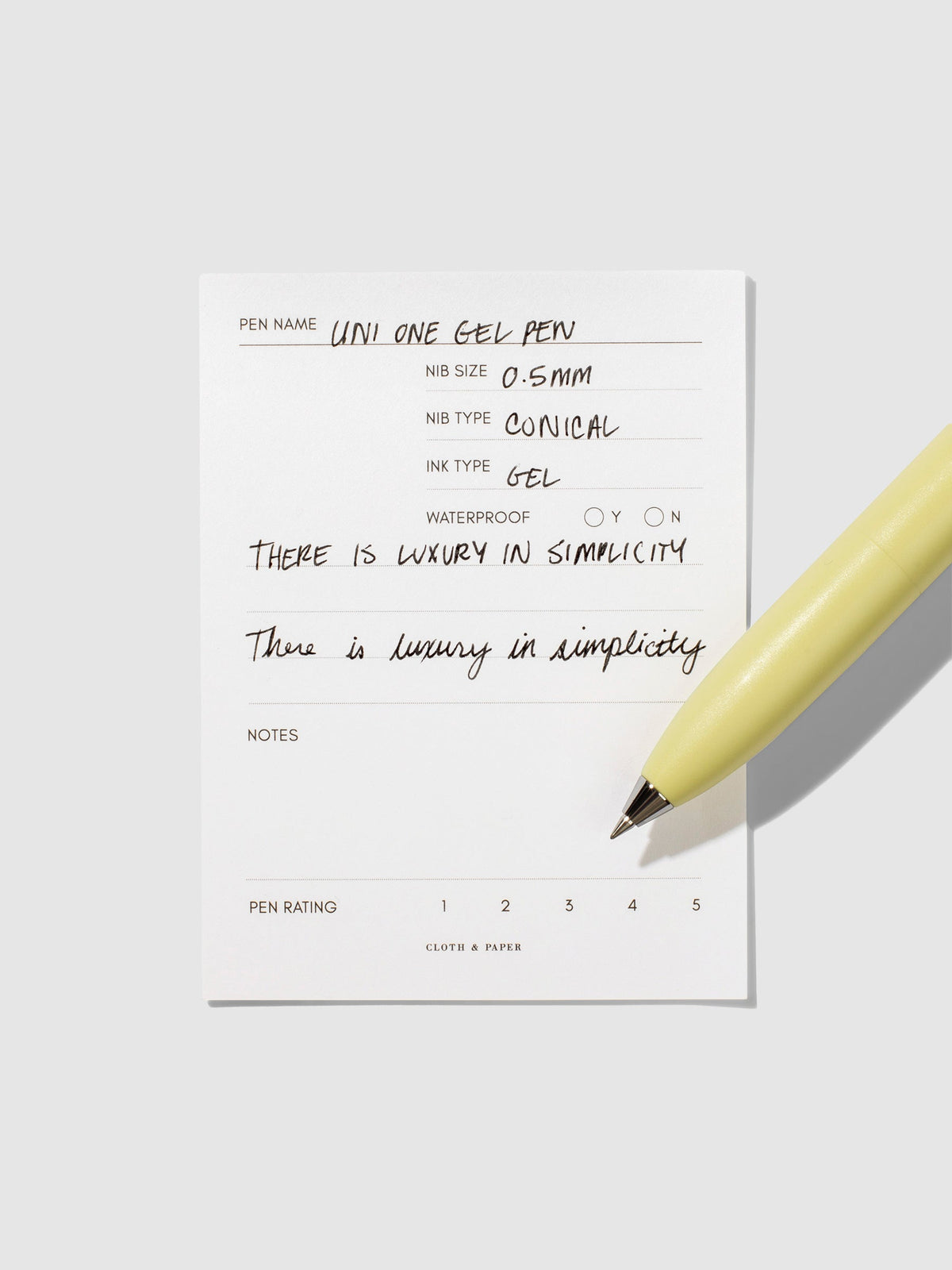 Uni-Ball One P pen resting on a pen test sheet. The sheet shows the pens specs. Color pictured is Banana.