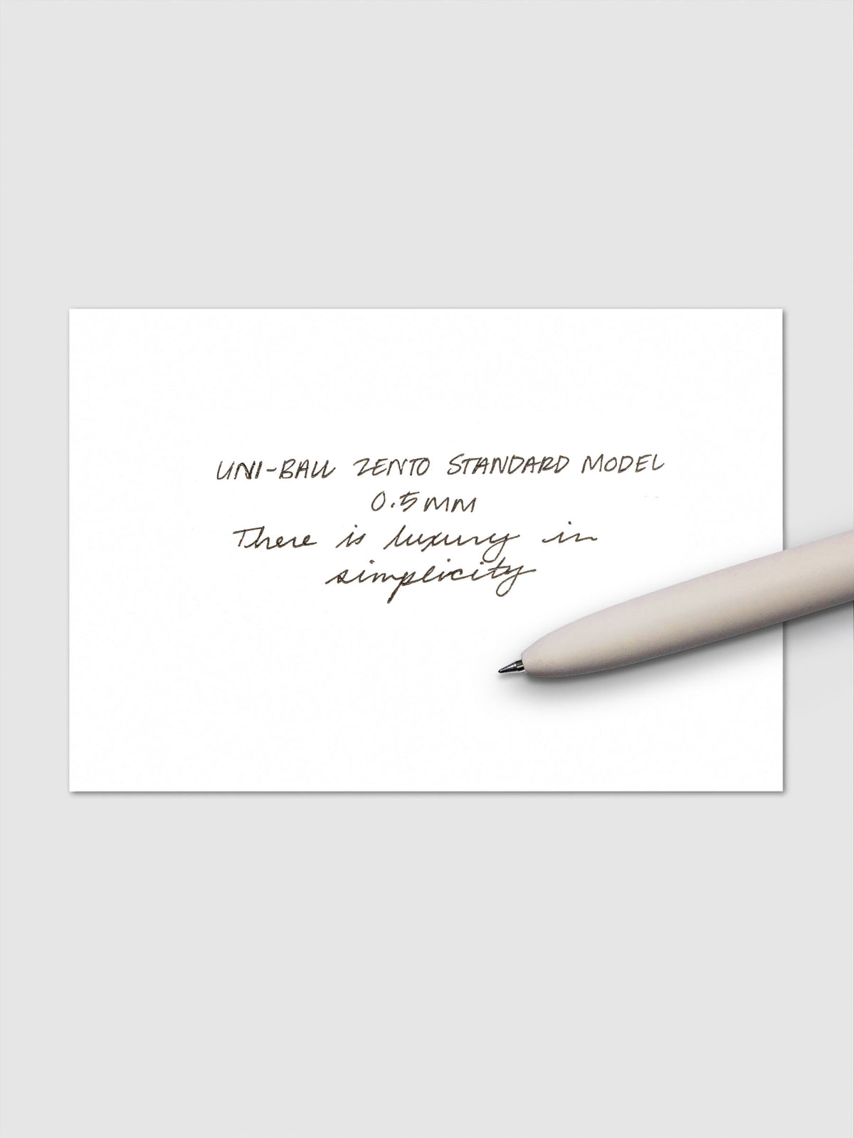 Handwritten sample using the Uni-ball Zento Standard Model Pen with black ink and a 0.5 mm nib. Shown with off-white pen resting across paper.