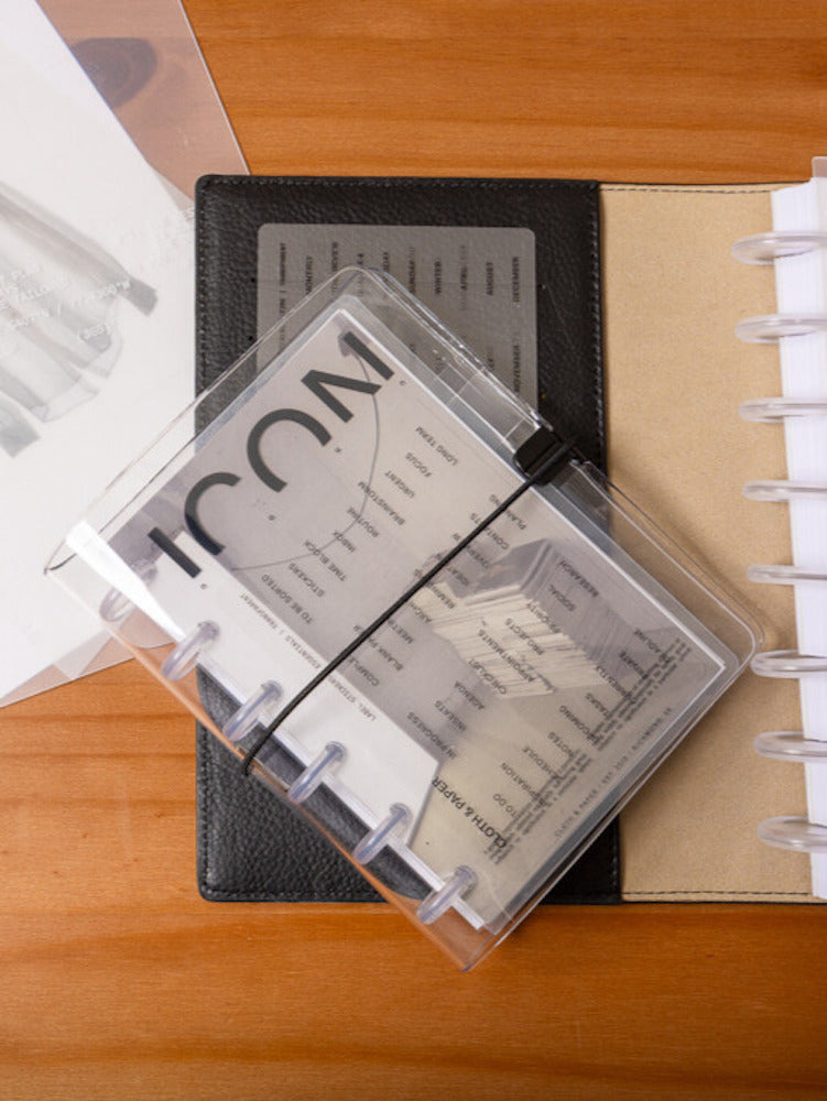 Clear Vinyl Planner Cover in size CP Petite shown with a CP Petite discbound planner inside on a wooden table with other Cloth & Paper products.
