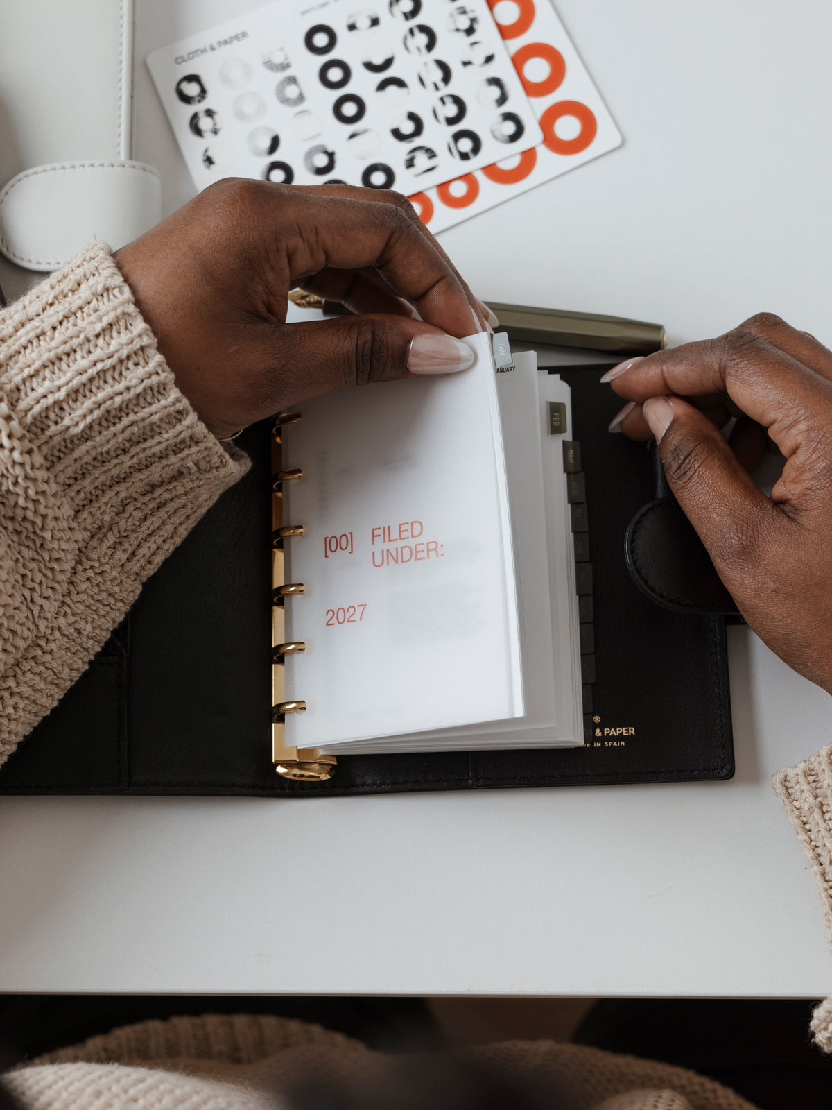 A top-down view of a person flipping through a 6-ring planner with a frosted translucent dashboard in Rouge colored text.