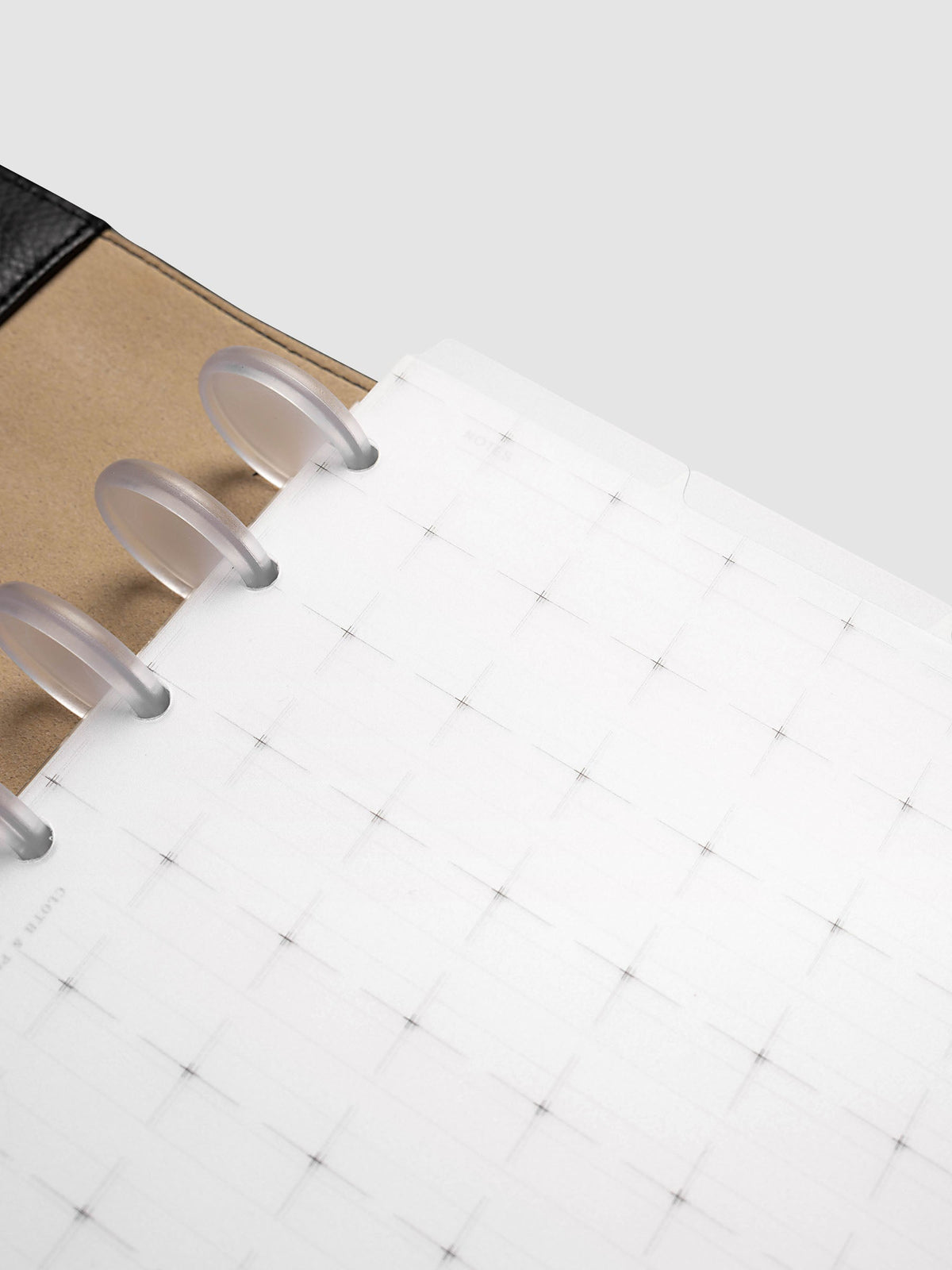 Grid Top Tab Dividers | Ultra-Thin, Half Letter 8-Disc Punch, angled close-up of three frosted clear discs holding the divider in place, with the notched edge and grid print in focus