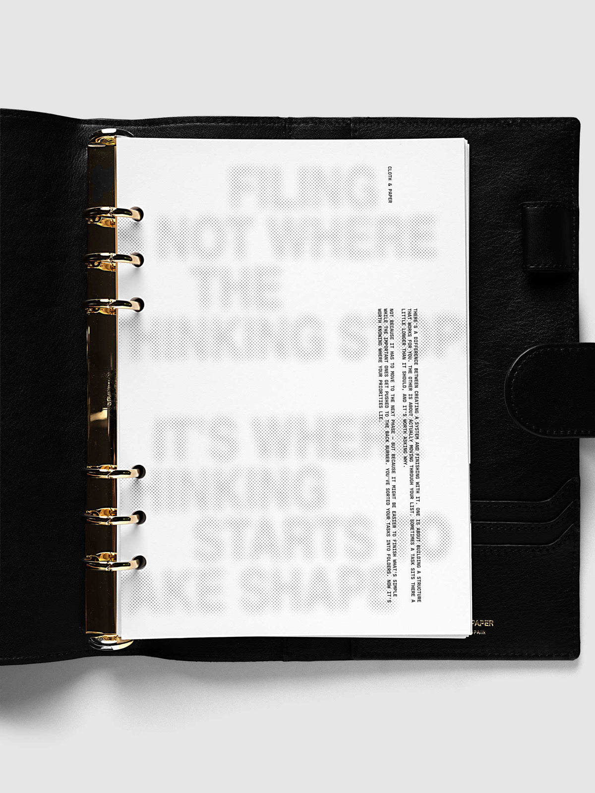 Halftone Planner Dashboard, A5 6-Ring Punch, dashboard on the gold rings of an open black leather planner, black typewriter text running down the right side
