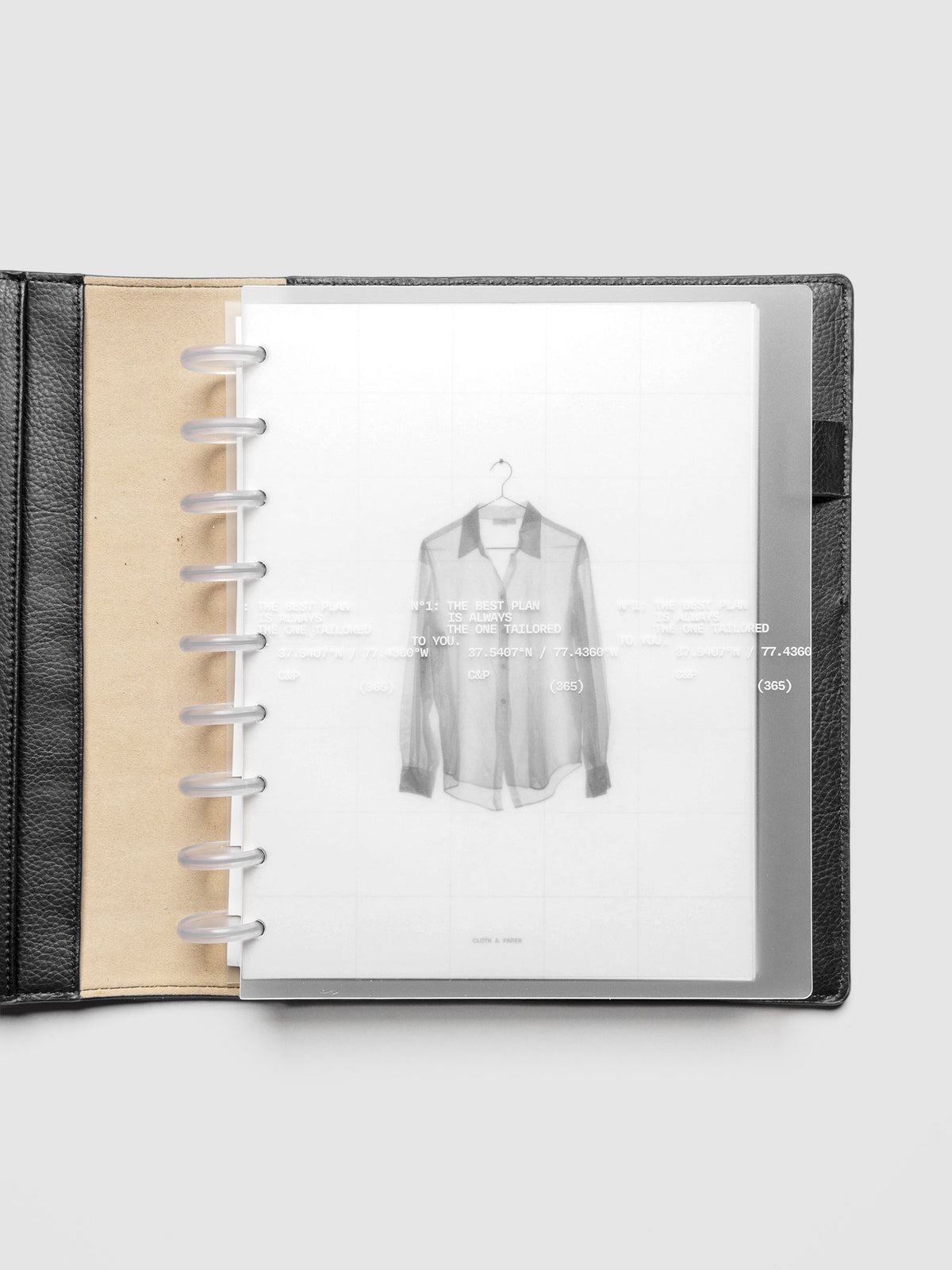 Transparent planner cover set with white printed text design and accompanying black and white dashboard with an image of a tailored shirt on a hanger. Shown discbound in a black leather folio in size HP Classic.